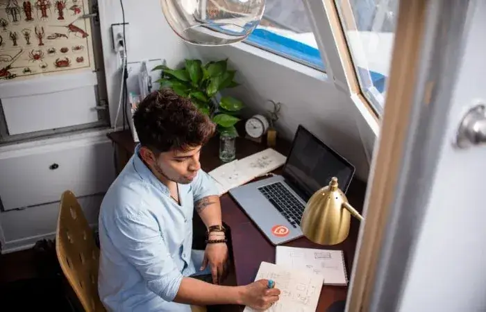 man working on laptop and writing on paper