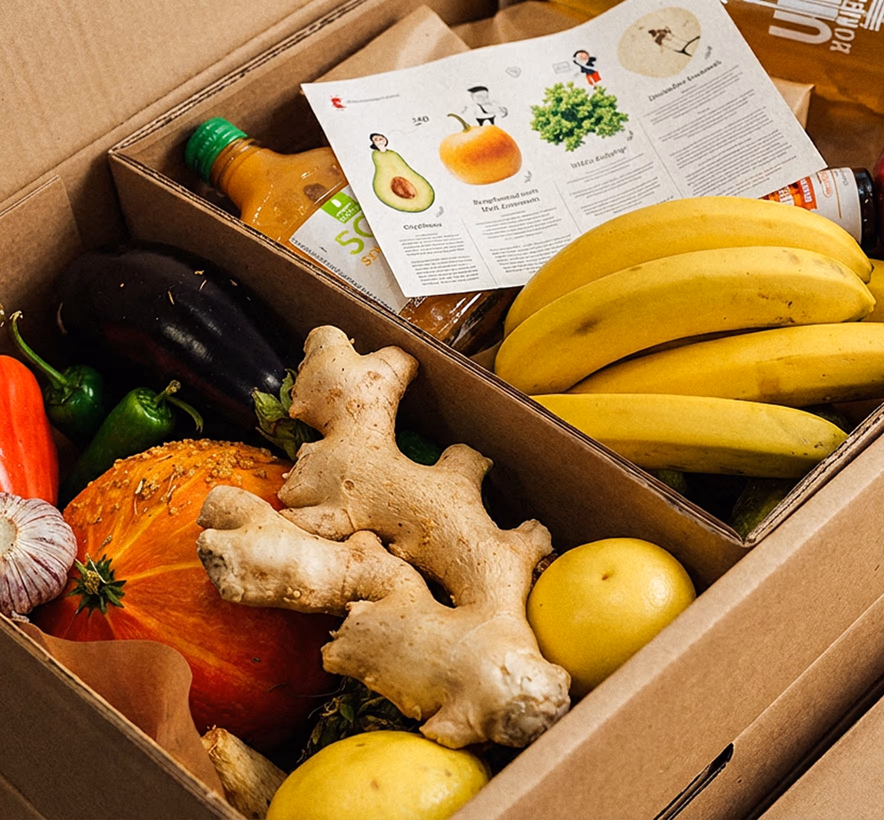 Pudełko z różnorodnymi świeżymi warzywami i owocami, m.in. bananami, imbirem i dynią oraz butelką soku.