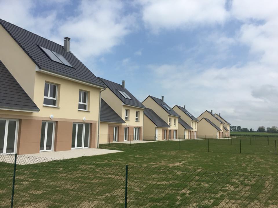 Une rangée de maisons modernes beiges à deux étages, avec des toits gris foncé et des panneaux solaires,