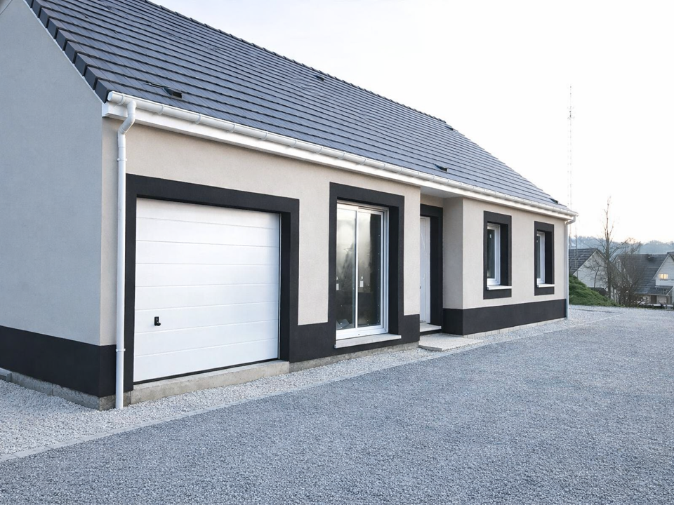 Maison moderne avec une façade grise et noire, une porte de garage blanche, plusieurs fenêtres et une allée en gravier.