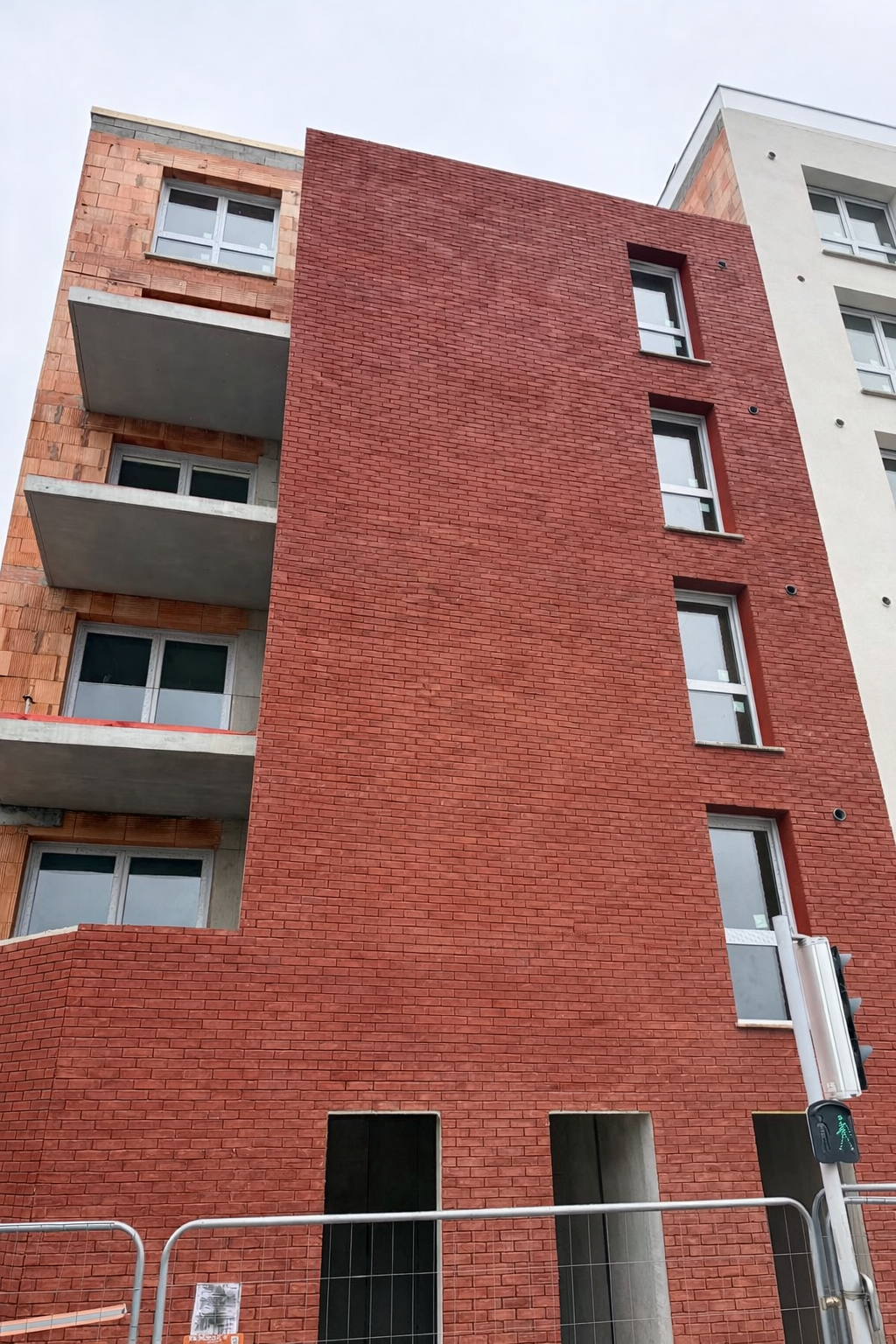 Immeuble à plusieurs étages partiellement construit, avec façade en briques rouges, et balcons en enduit.