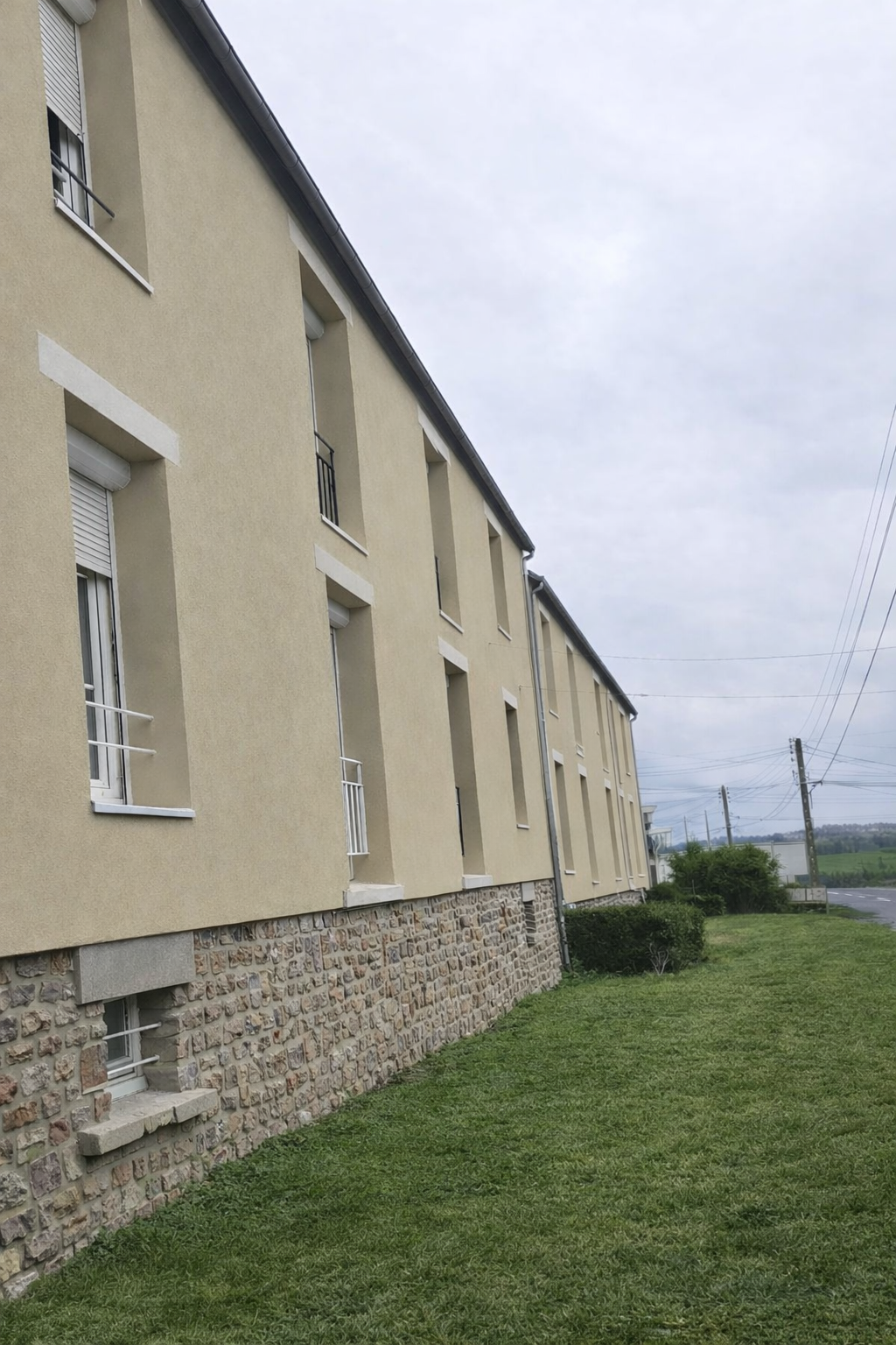Vue latérale d'un bâtiment beige aux fondations en pierre.