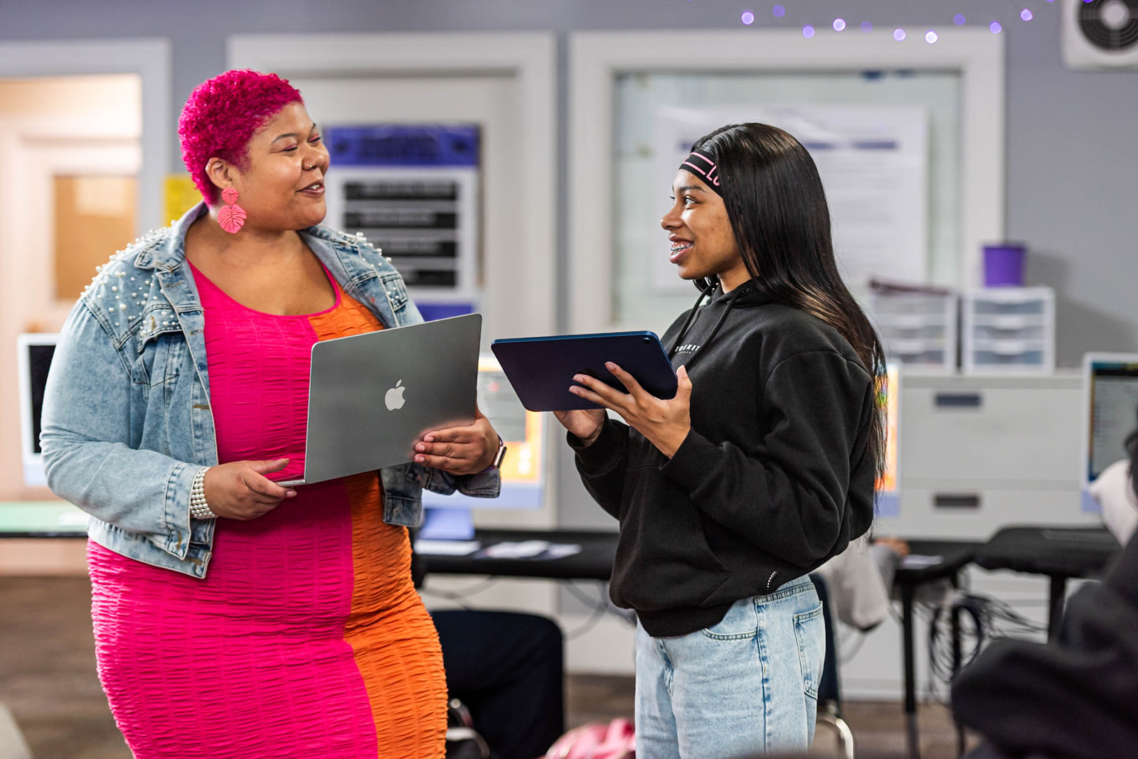 Two young people working together at a computer in a classroom setting.