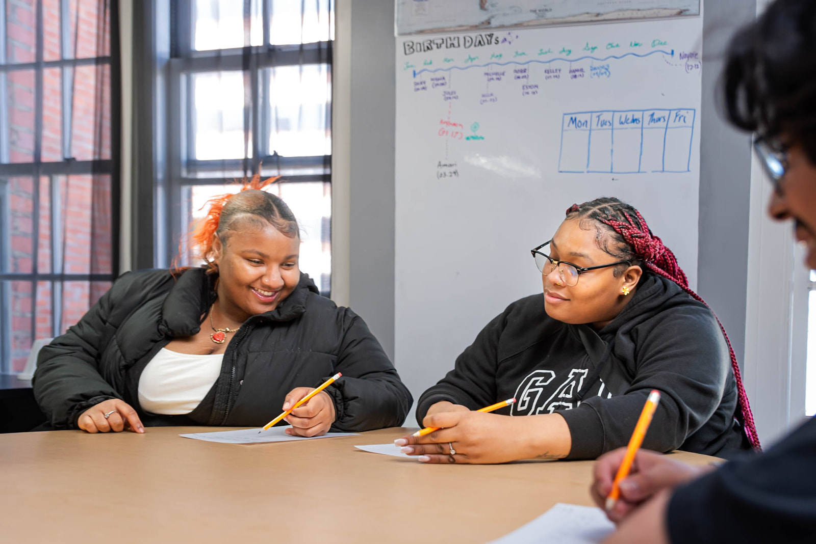 Young girl with curly hair wearing a black headband, focused on drawing with a blue colored pencil at a table with art supplies.