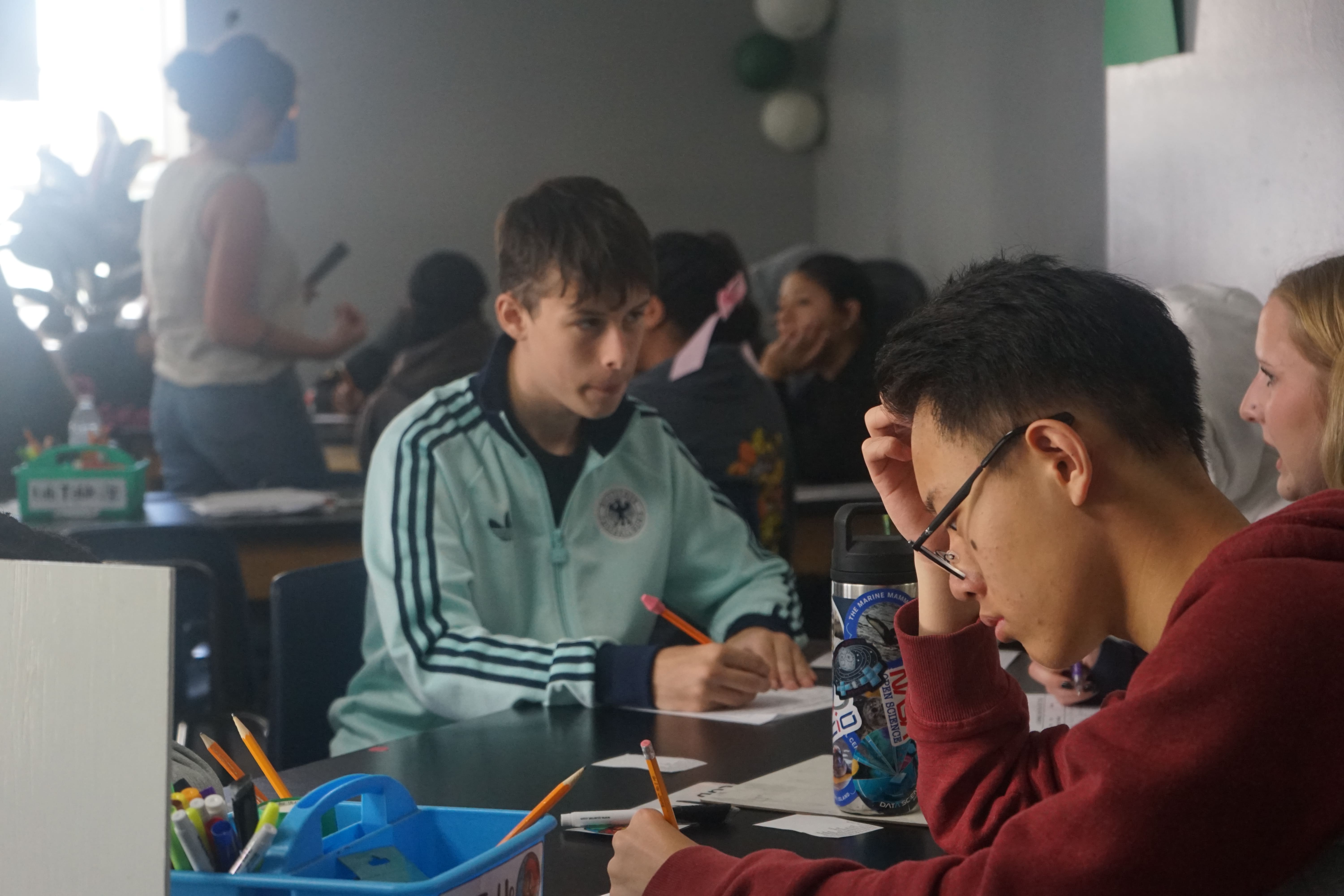 Three teenage boys sitting and smiling in a classroom holding copies of the book El Alquimista.
