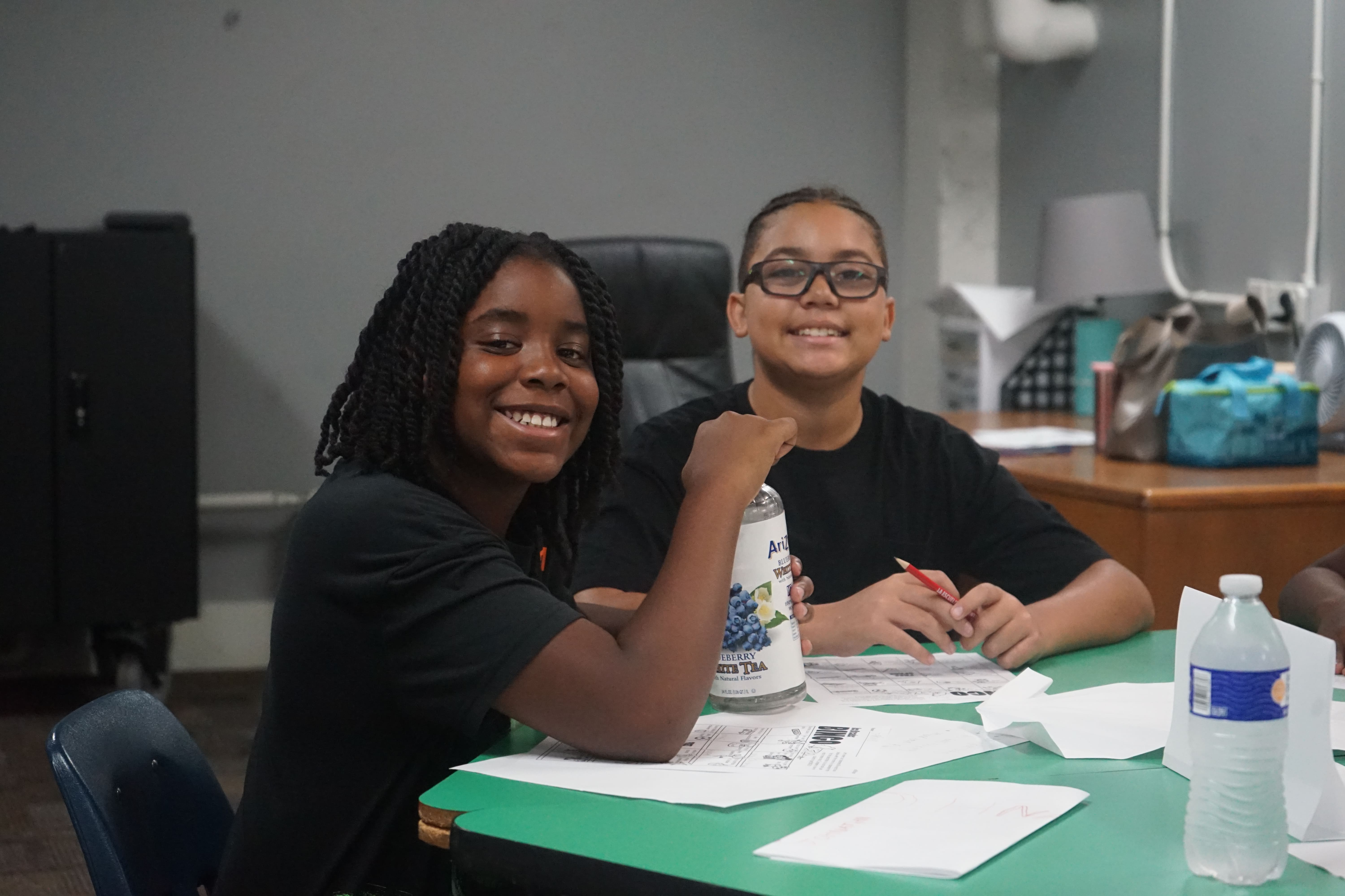 Two women collaborating on a project at a desk with papers and a pencil, smiling and focused.