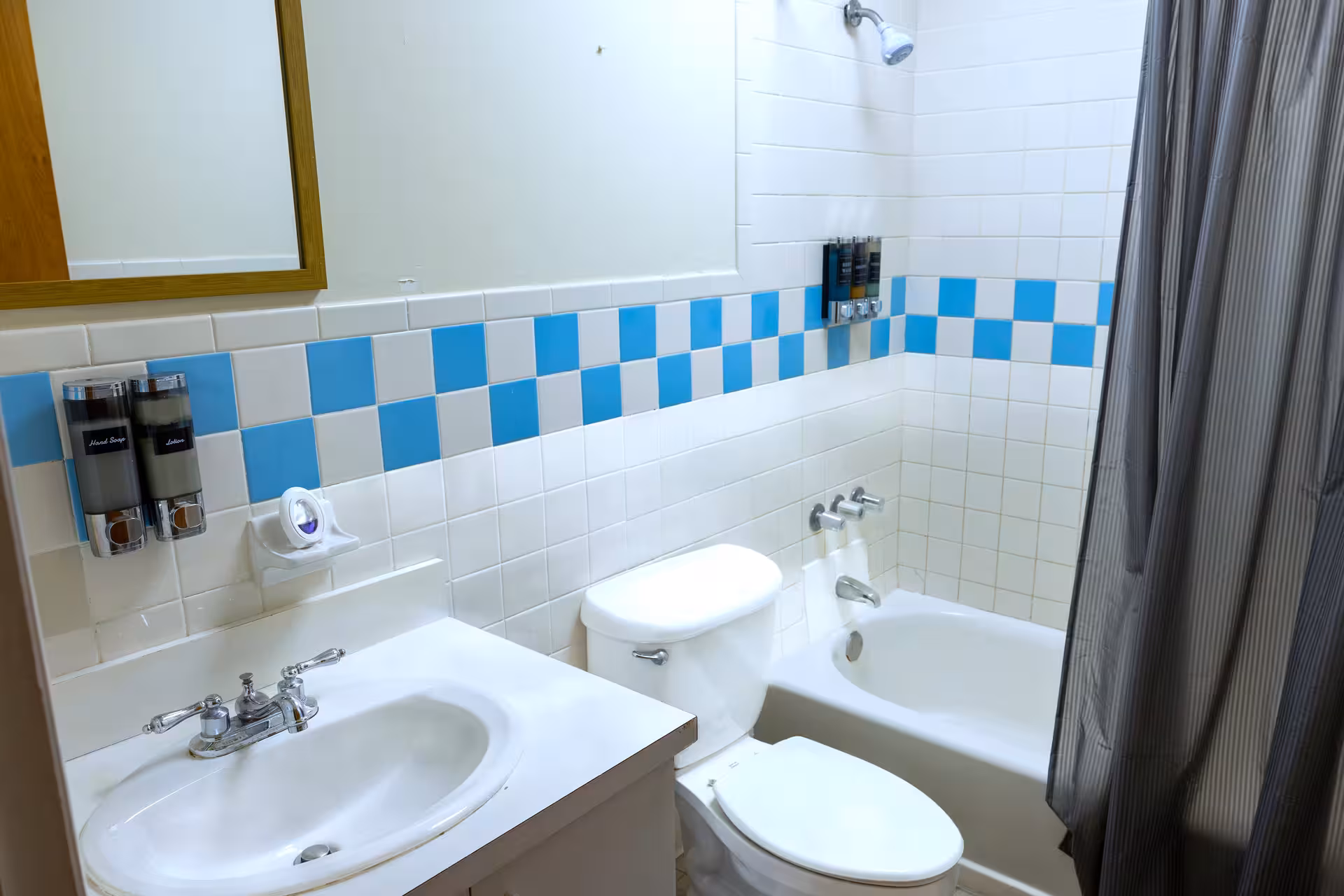 Small bathroom with white sink, toilet, bathtub, blue and white checkered tile wall, and gray shower curtain.