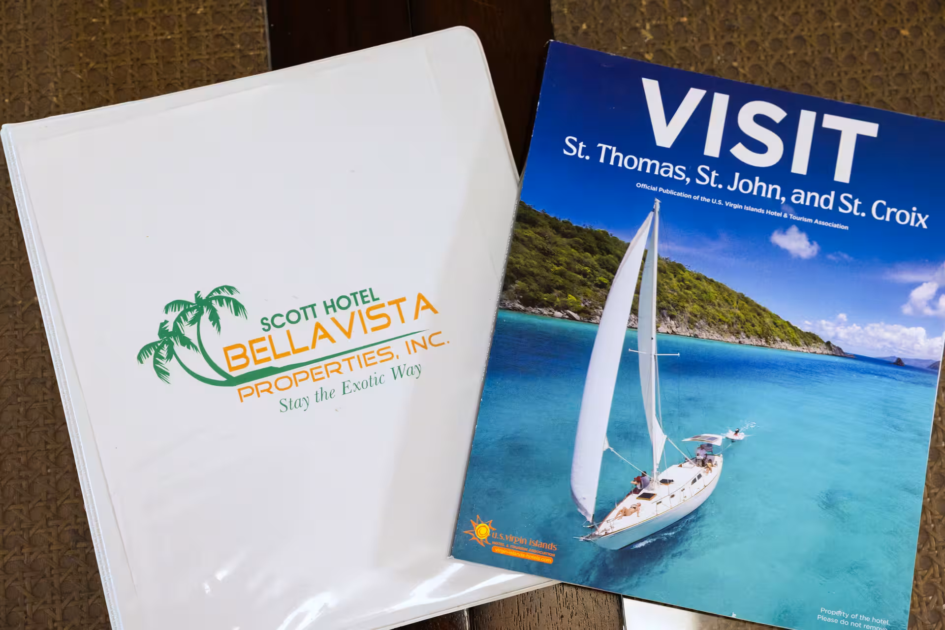Travel magazine titled 'VISIT St. Thomas, St. John, and St. Croix' with a cover image of a sailboat on clear blue water near a green island, next to a binder labeled Scott Hotel Bella Vista Properties.