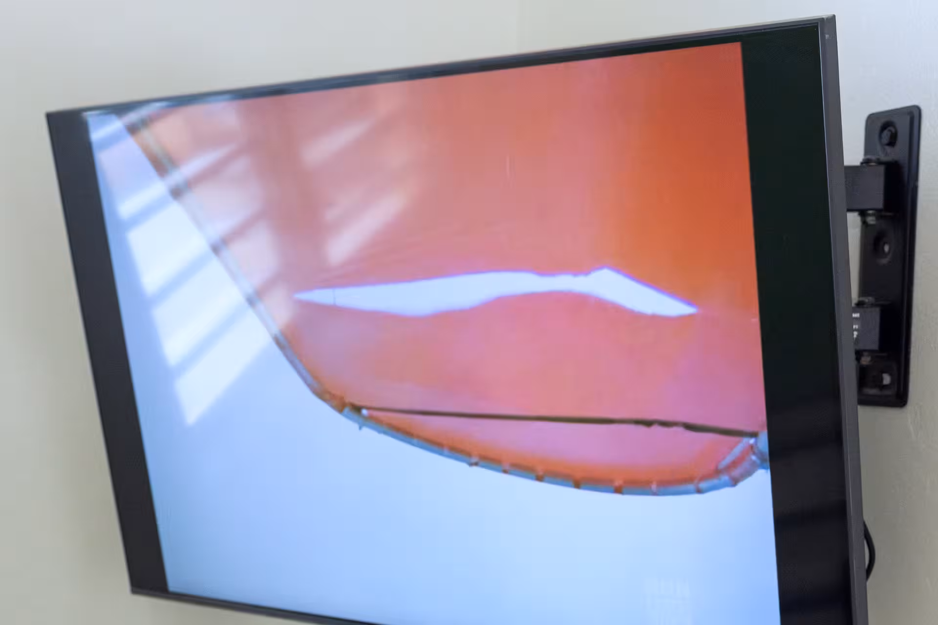Wall-mounted flat-screen TV displaying a distorted orange and white abstract image with reflections.