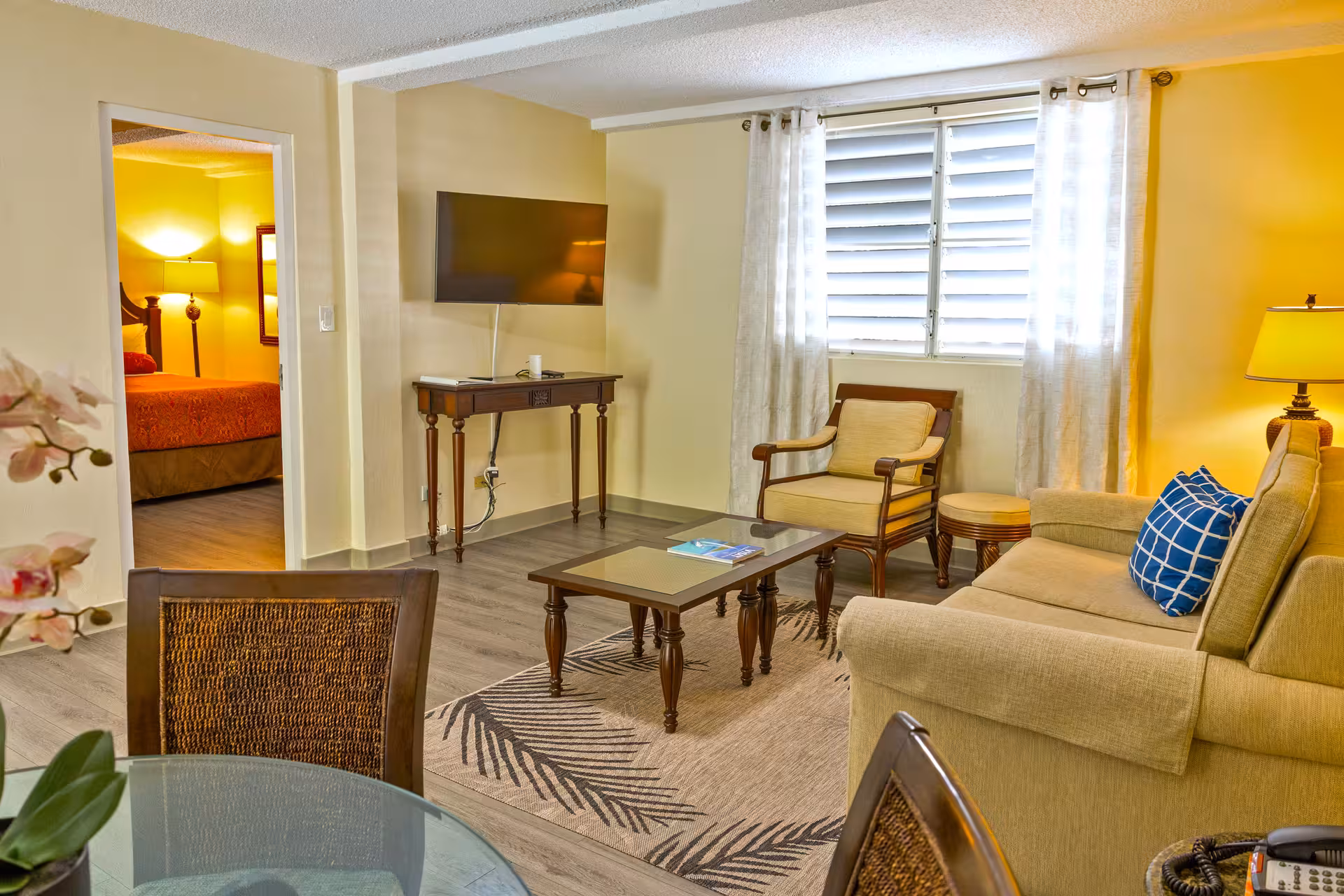 Cozy living room with beige sofa, armchair, wooden coffee table, flat-screen TV, and window with white curtains.