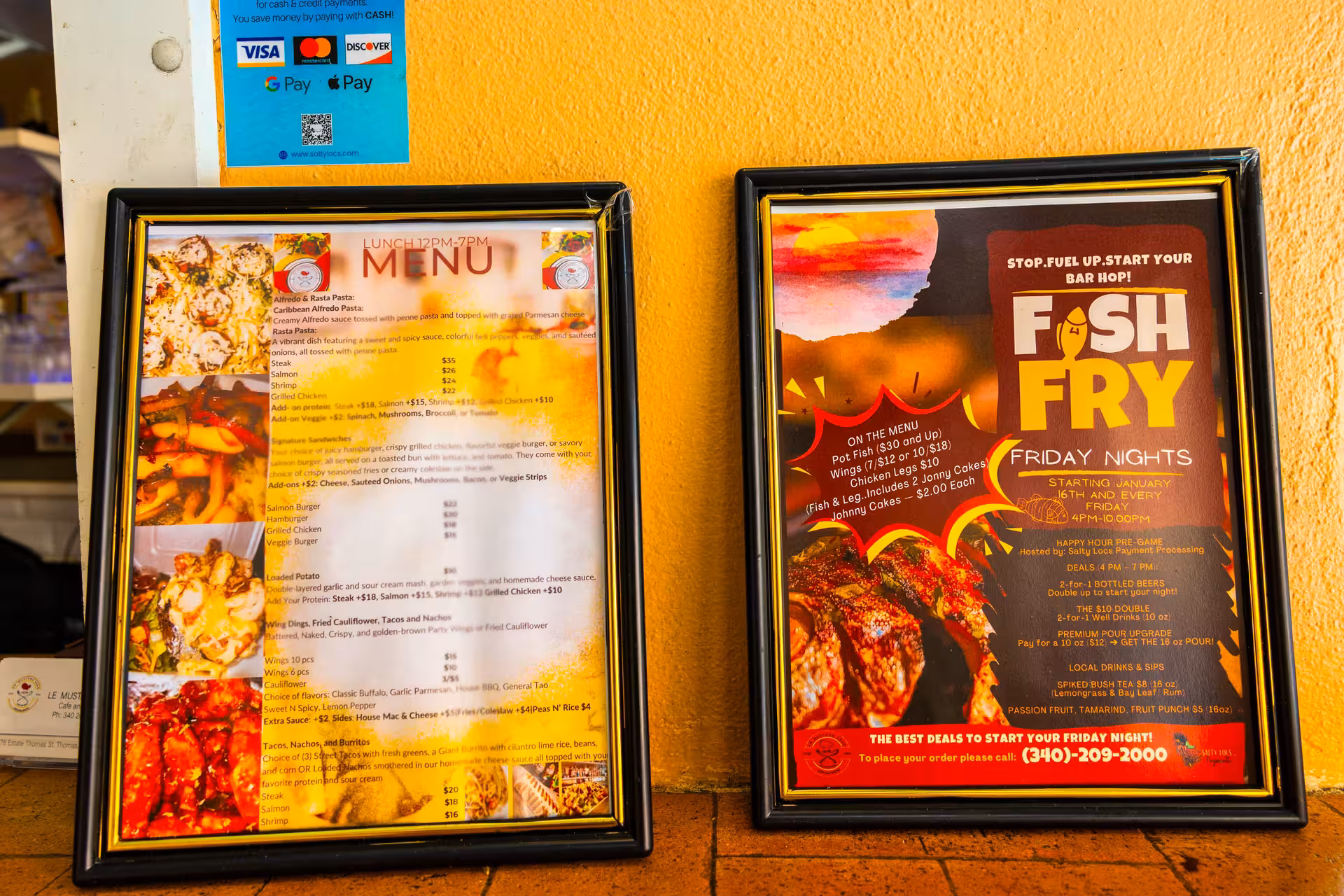 Two framed restaurant menus displayed side by side against a yellow textured wall, featuring pasta dishes on the left and a Fish Fry Friday Night event on the right.