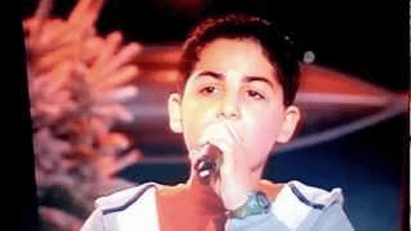 Young person holding and singing into a microphone on stage with blurred colorful background.