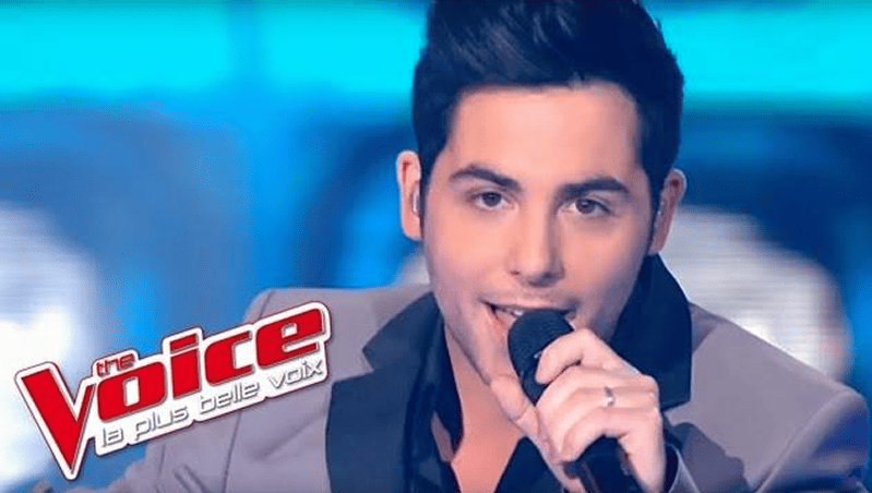 Male contestant singing with microphone on the stage of 'The Voice: la plus belle voix'.