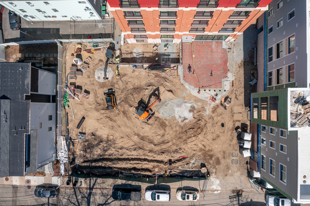 Aerial view of a construction site with heavy machinery, workers, and adjacent buildings.