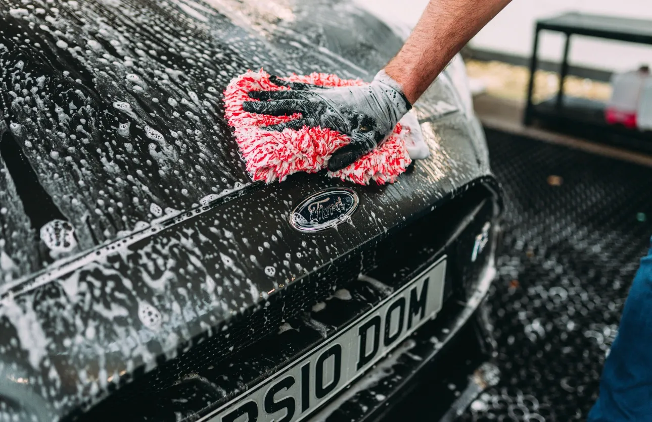 Hand wiping the headlight of a shiny black car with a red cloth.