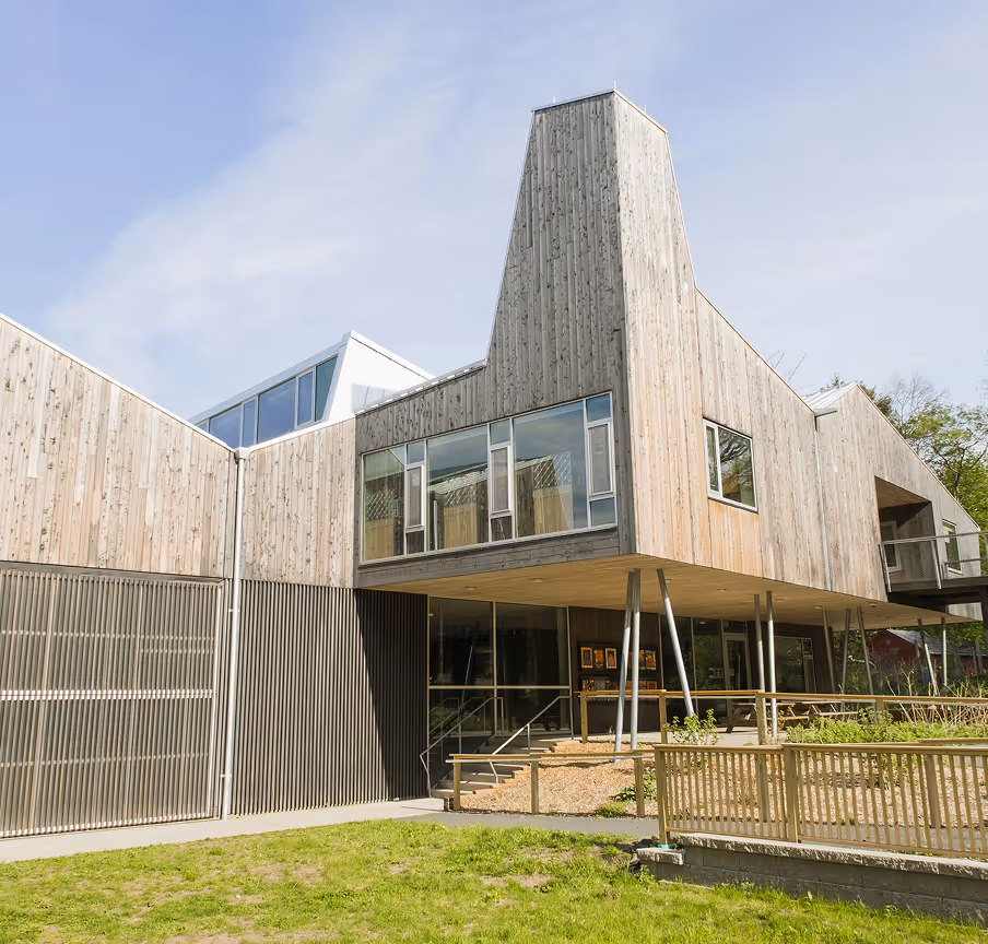 Modern building with wooden exterior and large windows elevated on metal pillars under a clear blue sky.