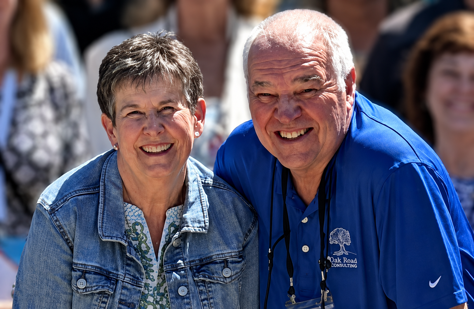 Smiling older man in blue shirt and woman in denim jacket posing together outdoors.
