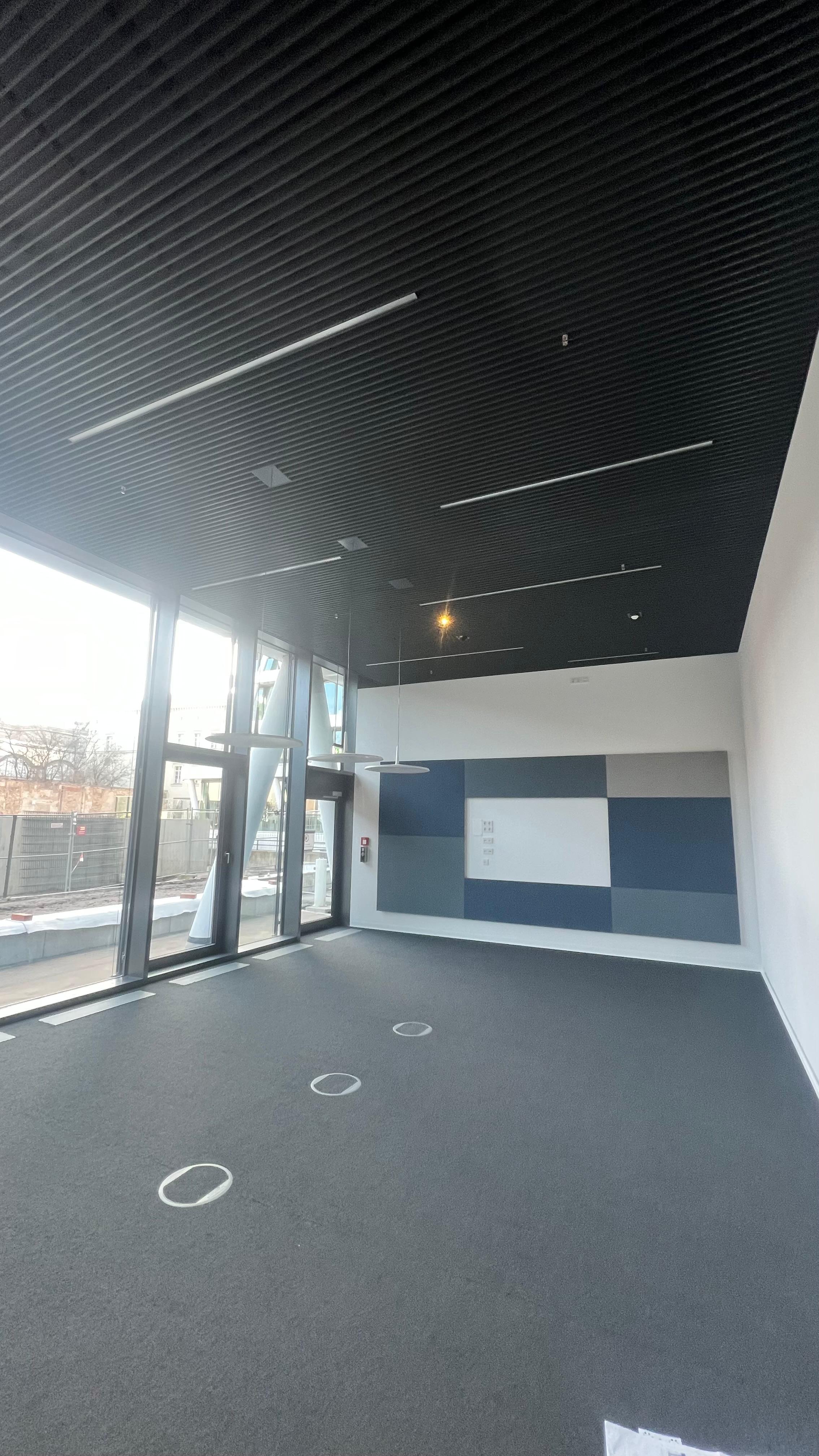 Fertiggestellter Innenraum mit schwarzer Bandrasterdecke, großen Fensterflächen und Wandpaneelen