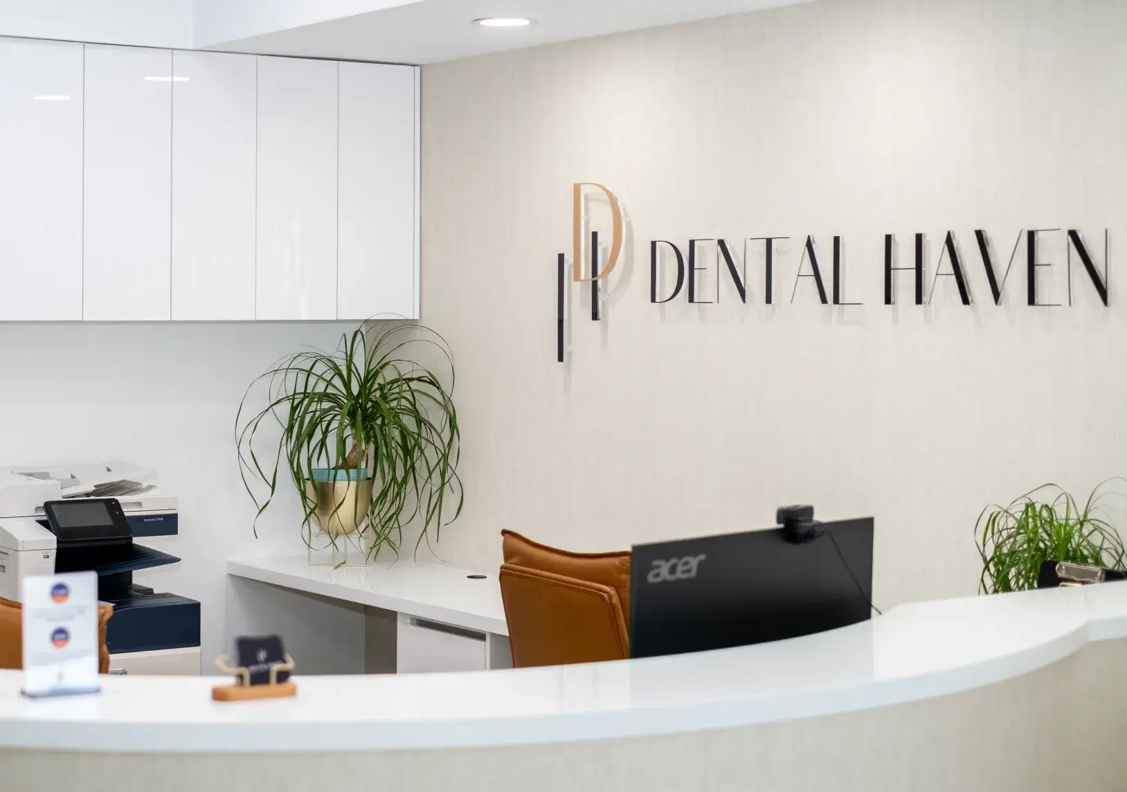 Reception desk at a dental clinic with a computer, office supplies, and a potted plant.