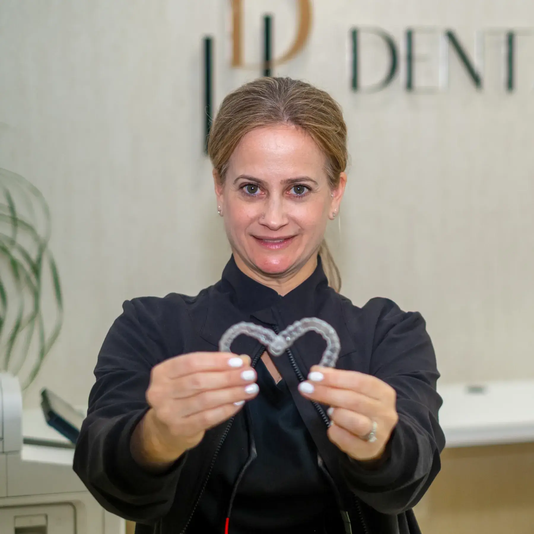 A woman holding a dental aligner, standing inside a dental clinic.