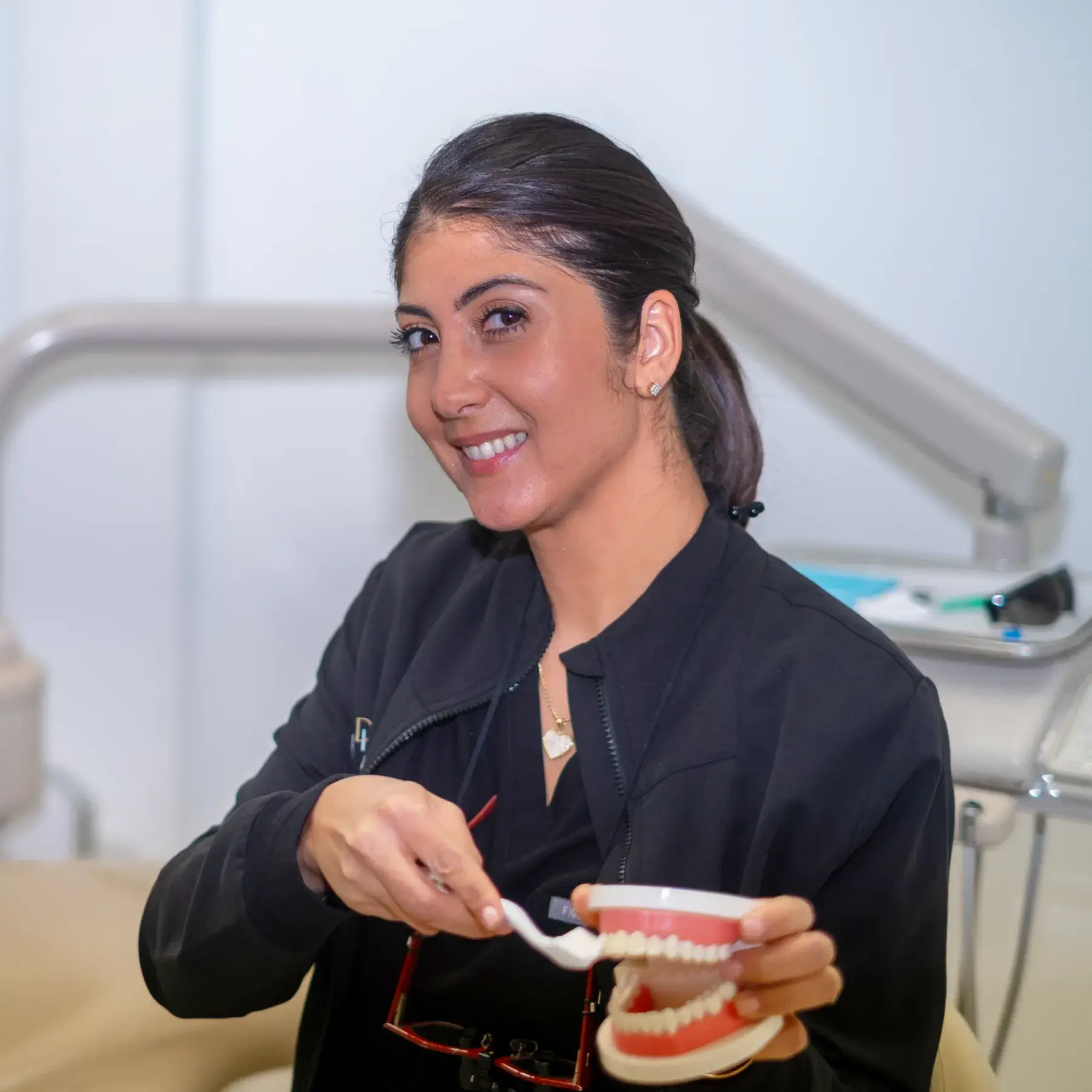 A person is demonstrating teeth brushing using a dental model in a dentist's office.