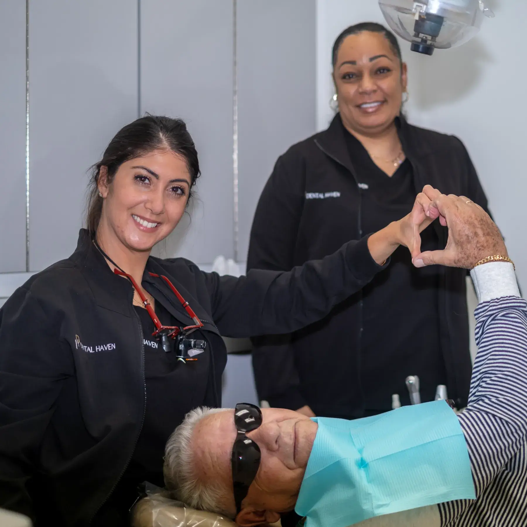 A dentist and patient smile, making a heart shape with their hands during a dental appointment.