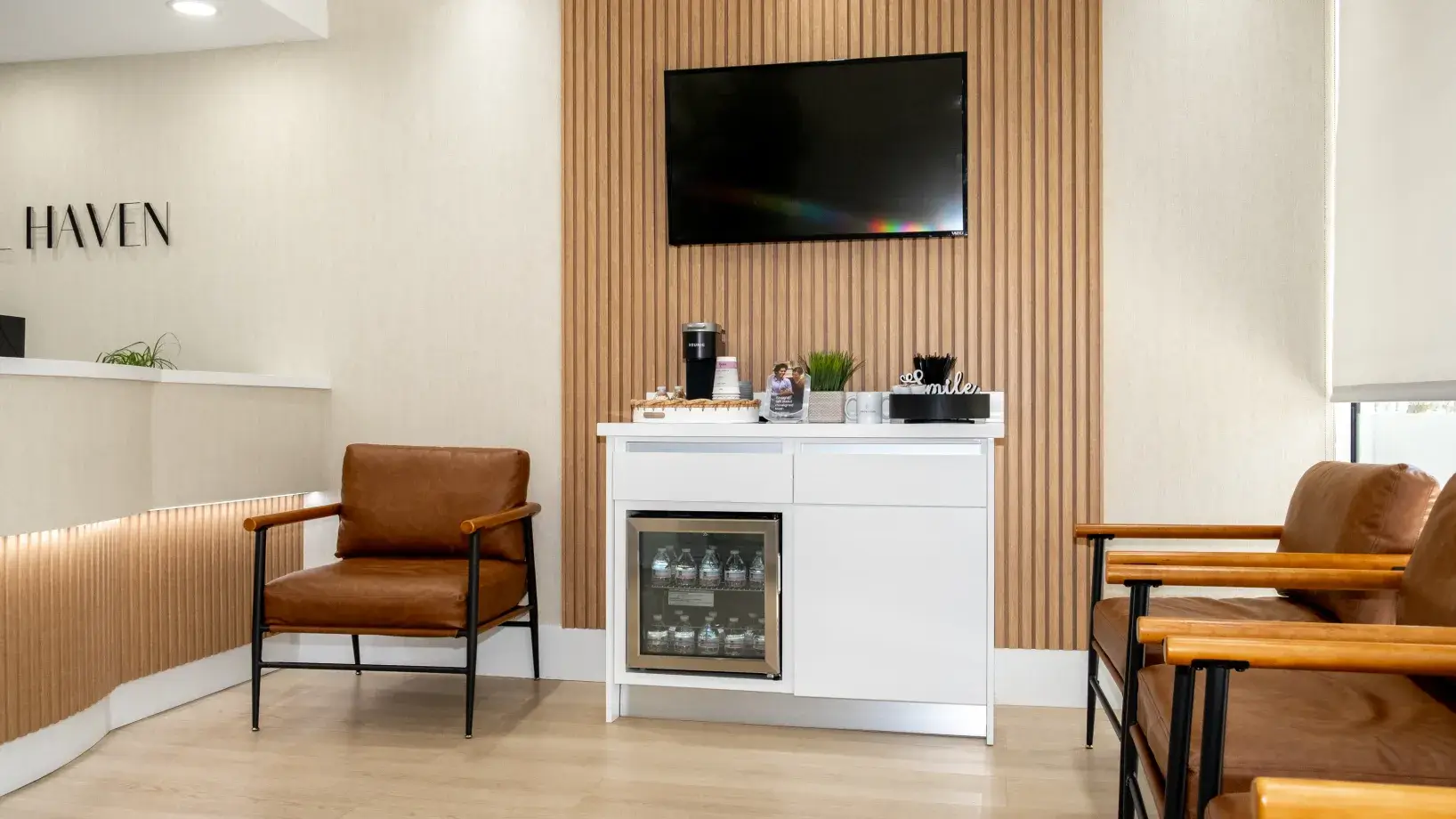 Reception area with two leather chairs, a TV on the wall, and a refreshment station.