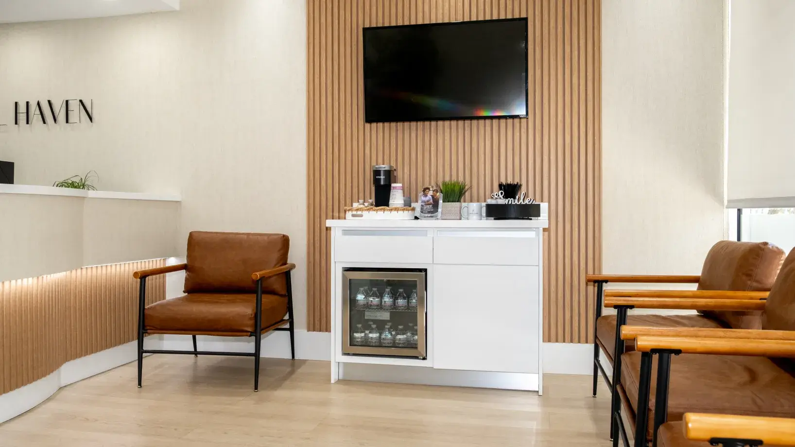 A waiting room with chairs, a wall-mounted TV, and a cabinet holding drinks and snacks.