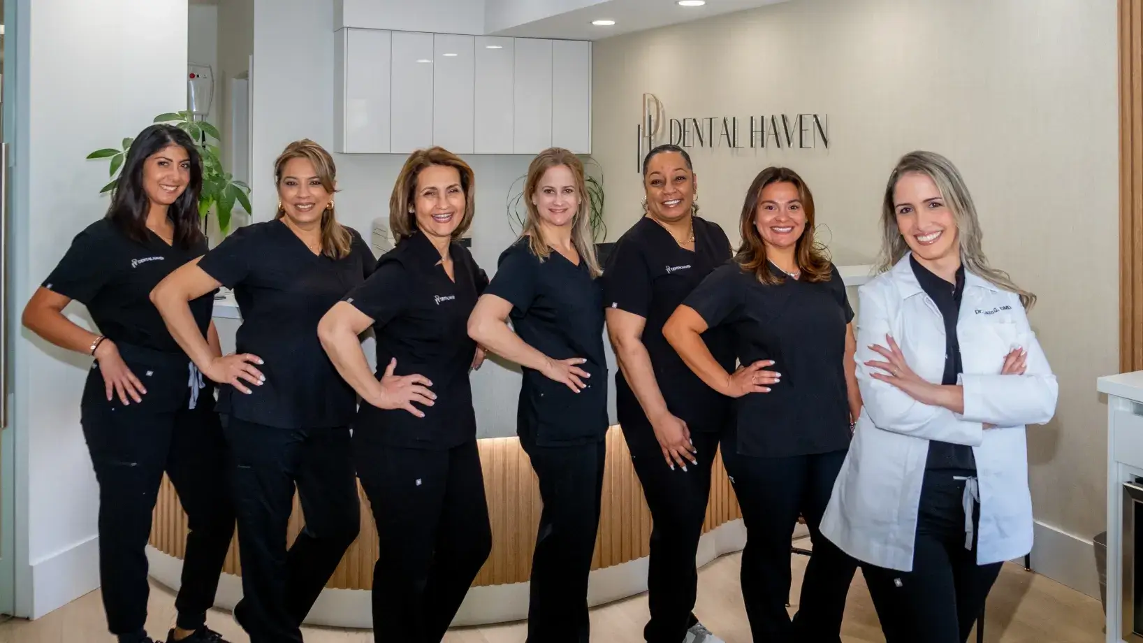 Seven dental staff members pose together in black uniforms, while one stands in a white coat.