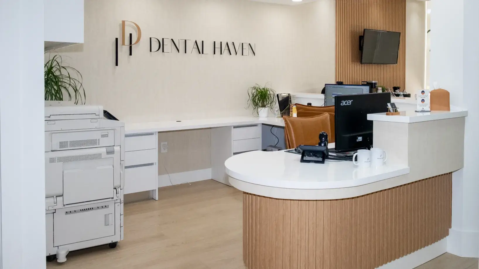 A modern dental office reception area with a counter, computer, and dental practice sign on the wall.