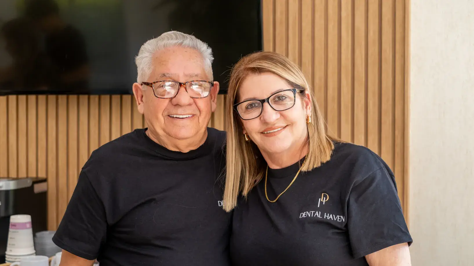 Two smiling people wearing matching Dental Haven shirts, standing together indoors.