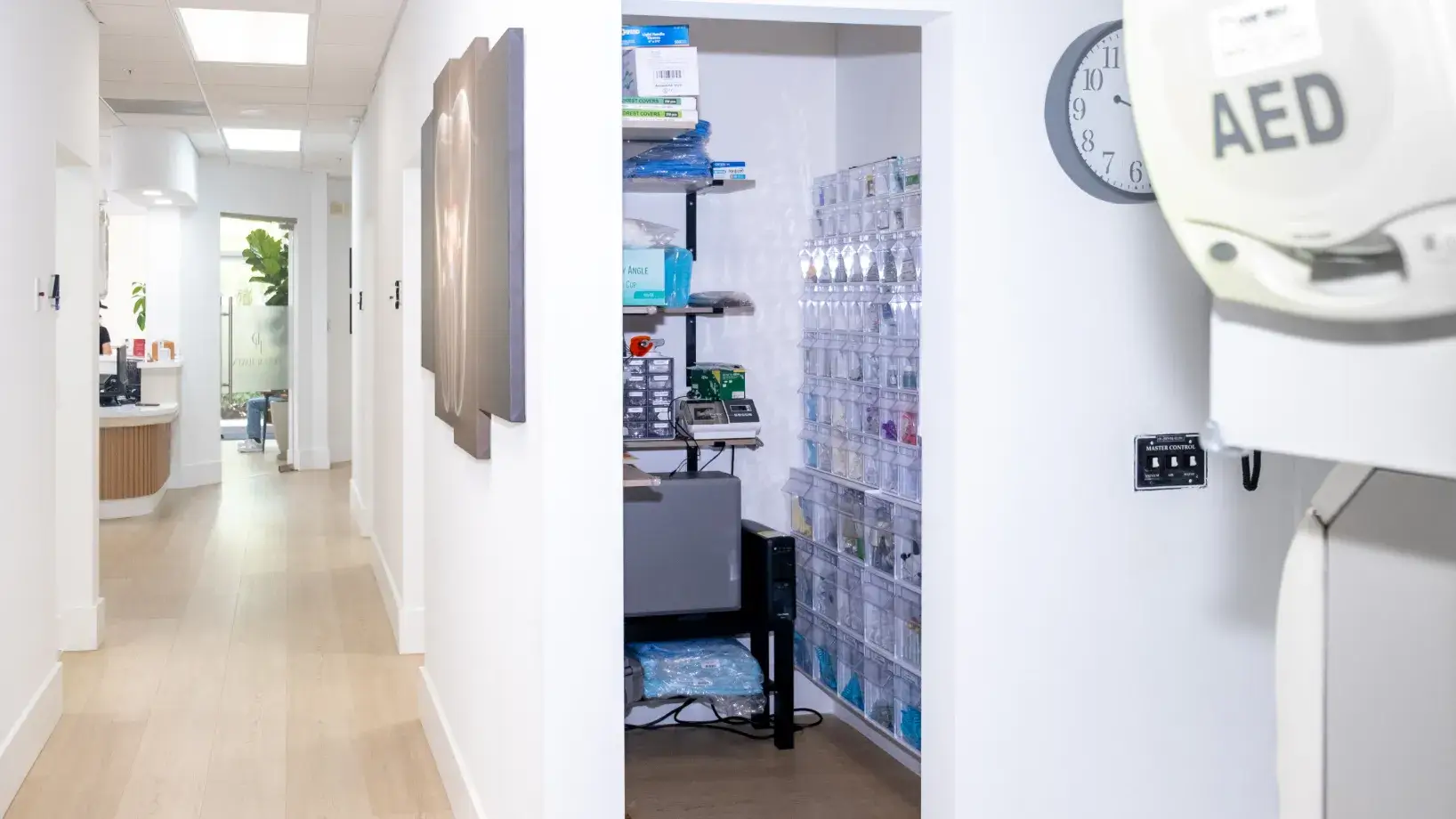 A hallway in a medical office with an AED device and a supply room nearby.