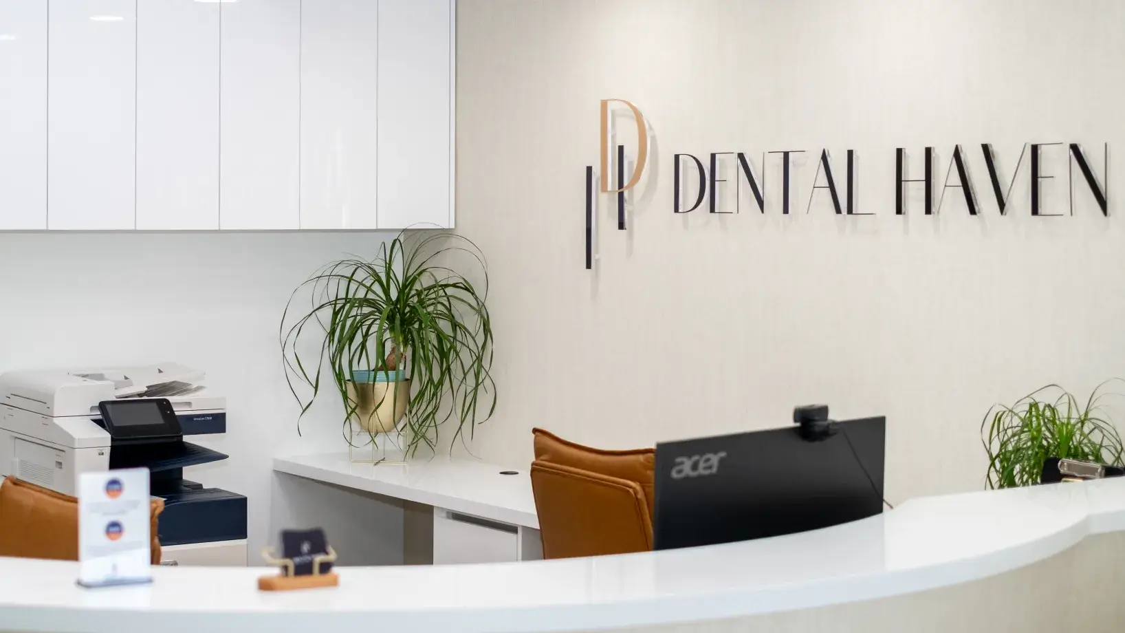 Reception desk in a dental office with a computer, printer, and plant. Sign reads "Dental Haven."