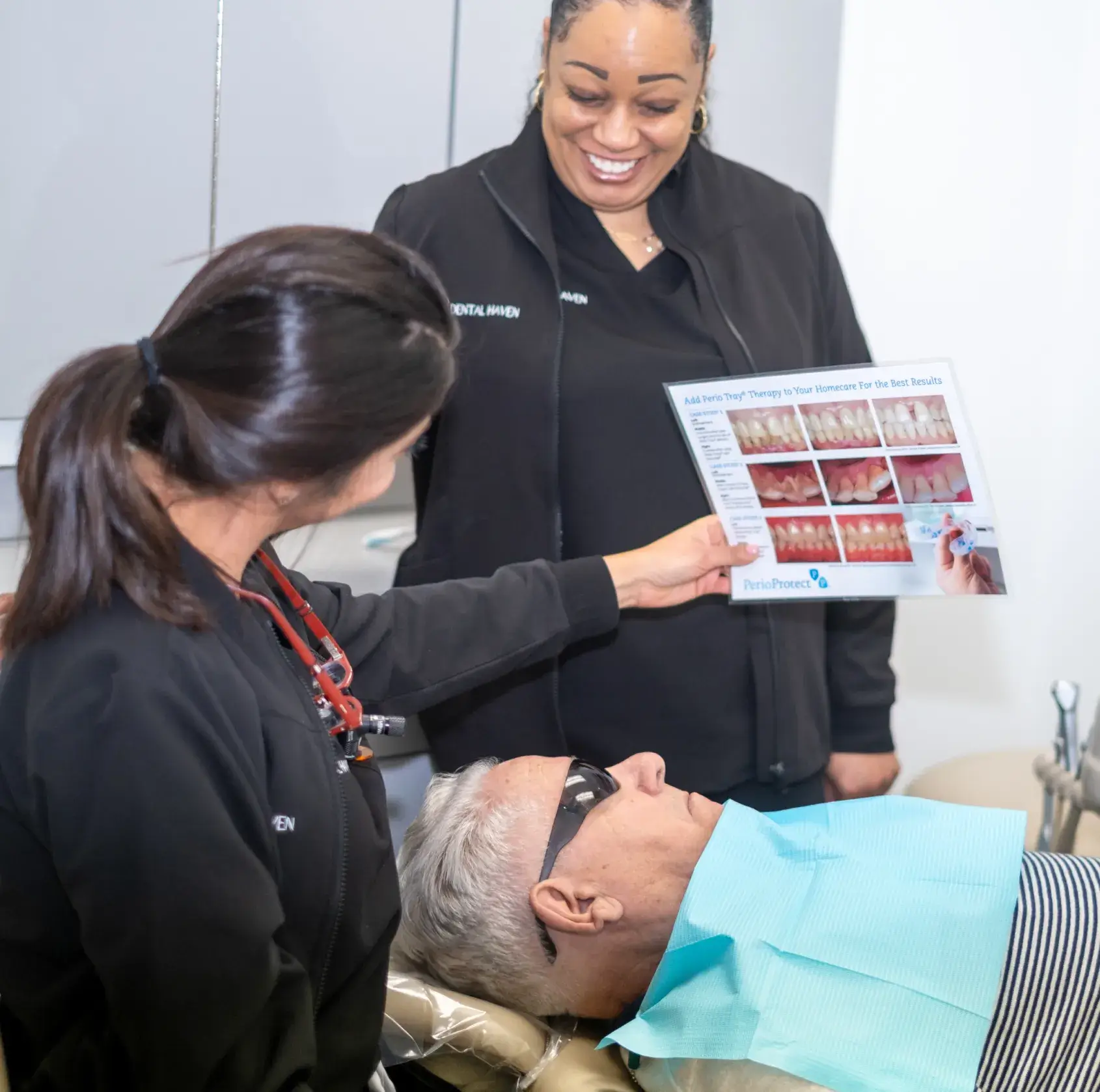 Two dental professionals show a patient a brochure while he sits in the dental chair.