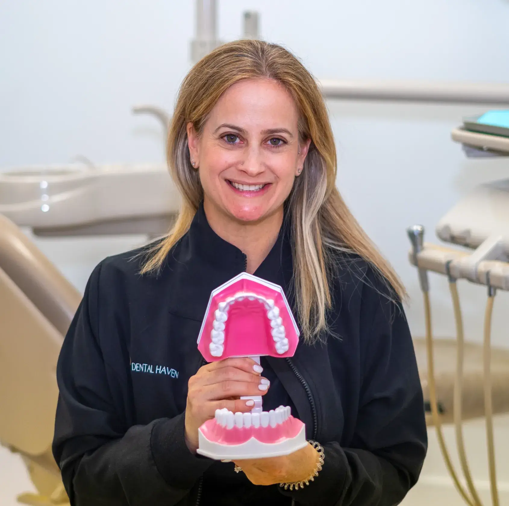 A woman holds a large dental model in a dental office.