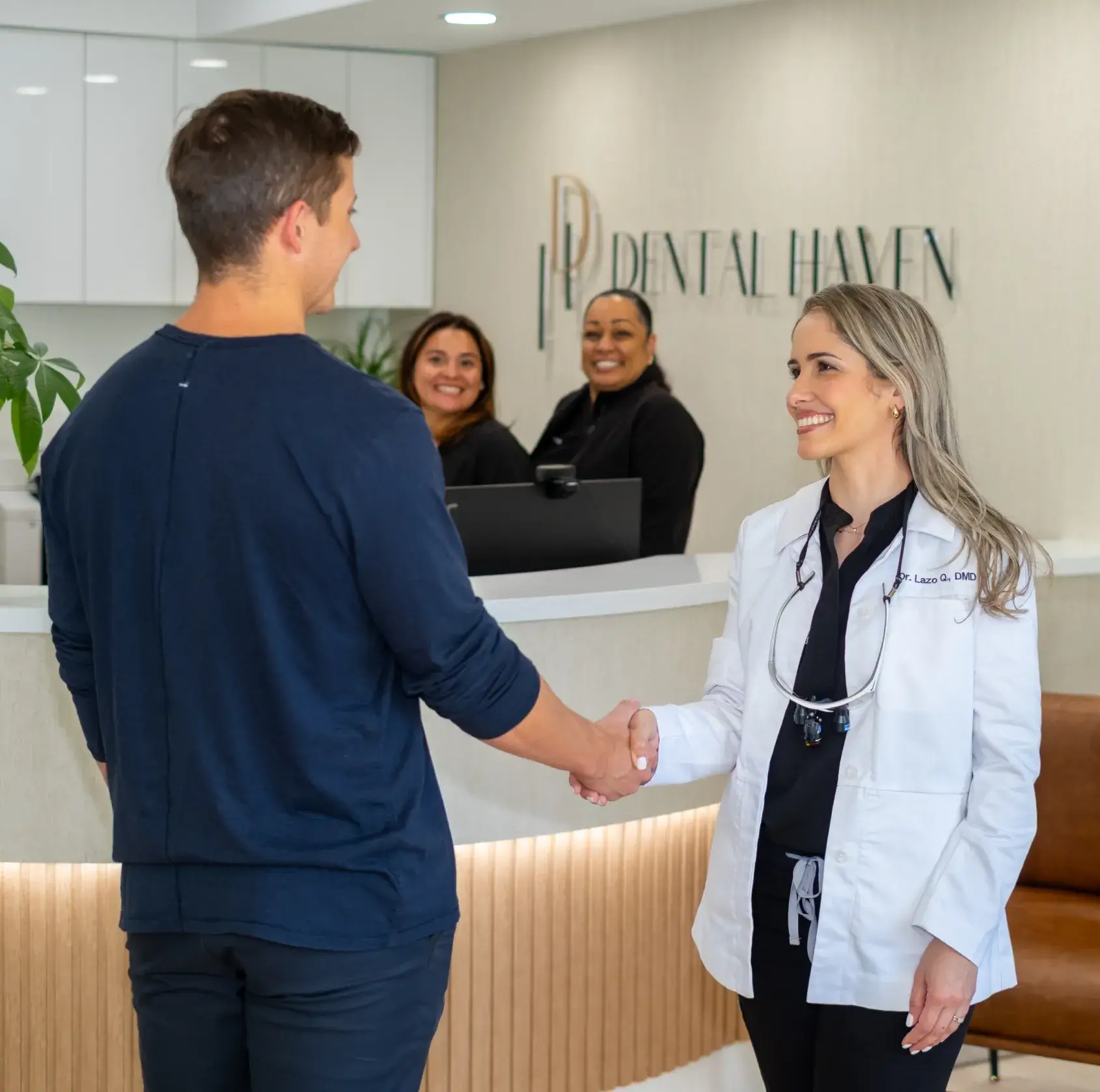 A dentist and a patient shake hands in a dental office, with staff smiling in the background.