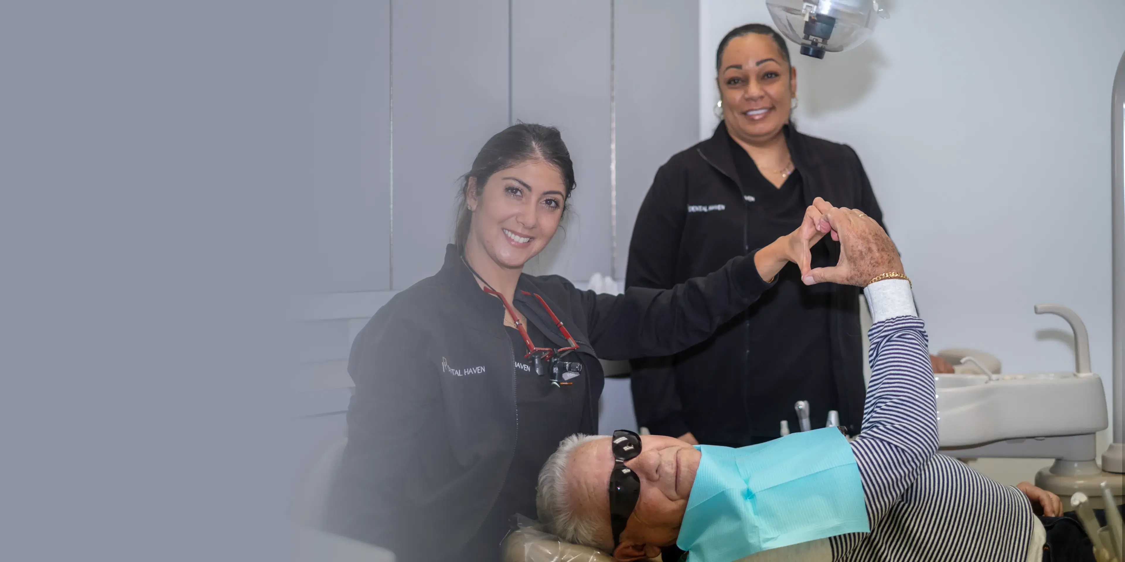 A dentist and assistant smiling while holding hands with a patient in a dental chair.