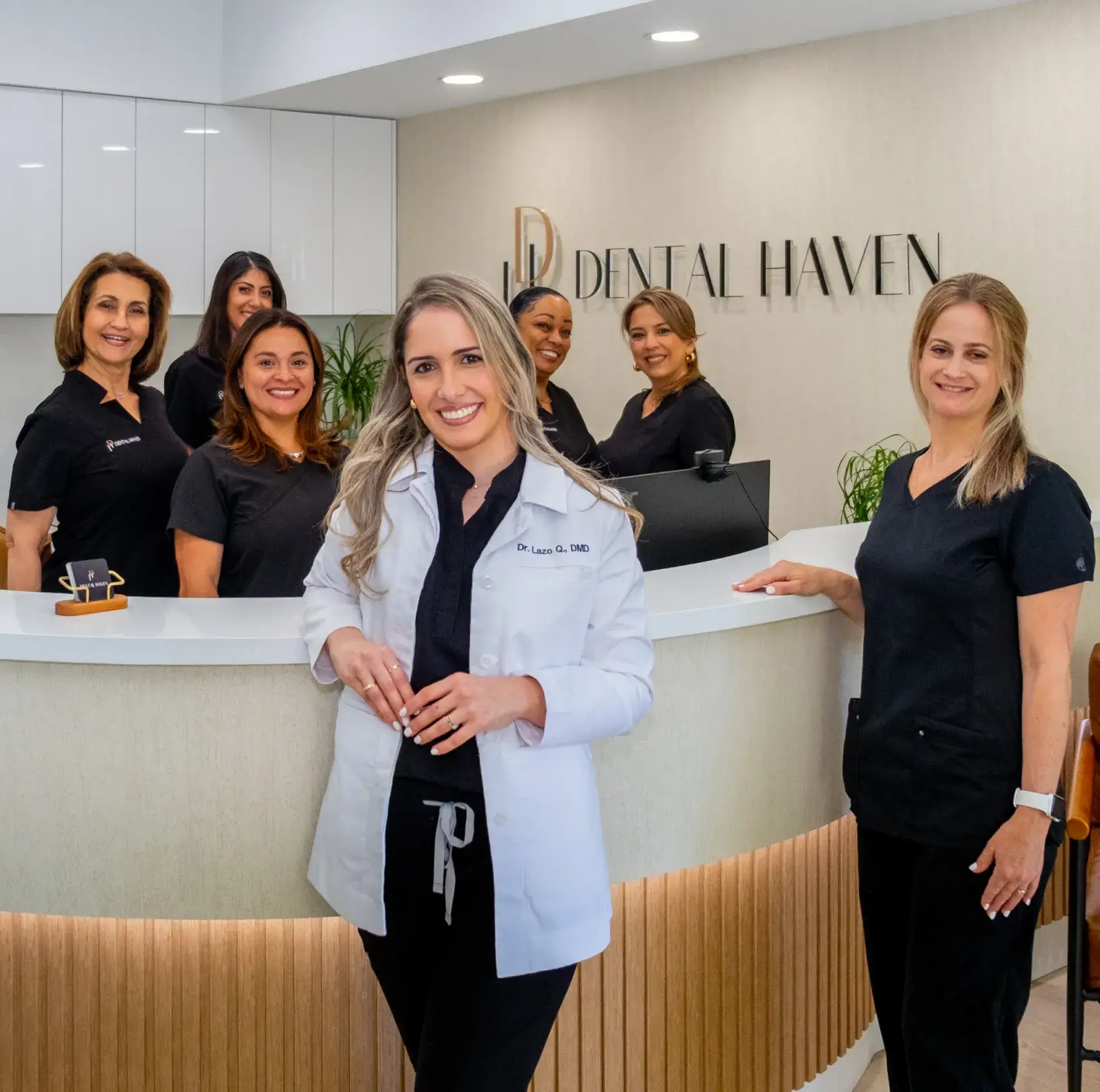 A group of dental professionals in uniforms pose together in a dental office reception area.