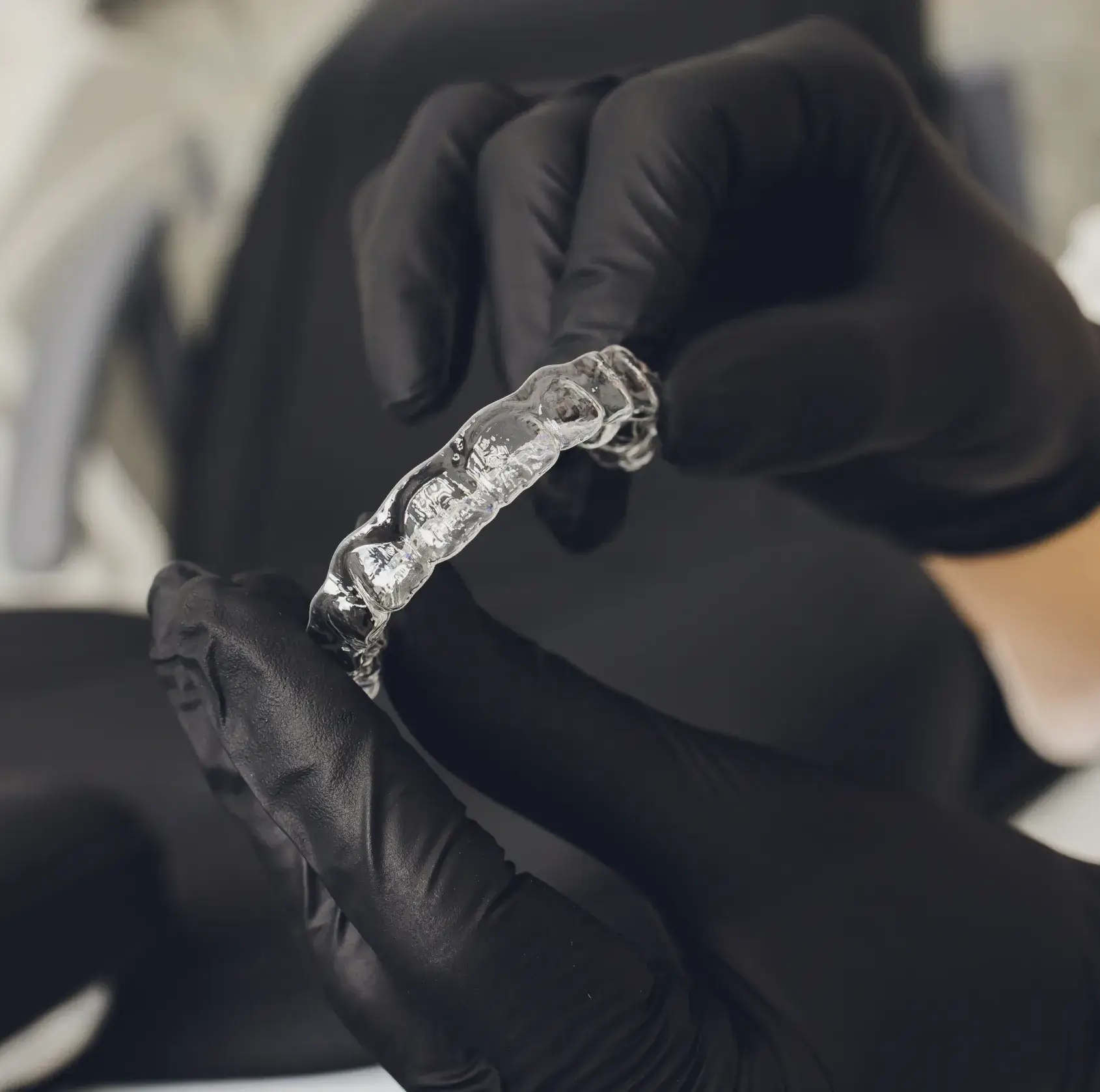 Gloved hands holding a clear dental retainer in a dental office.