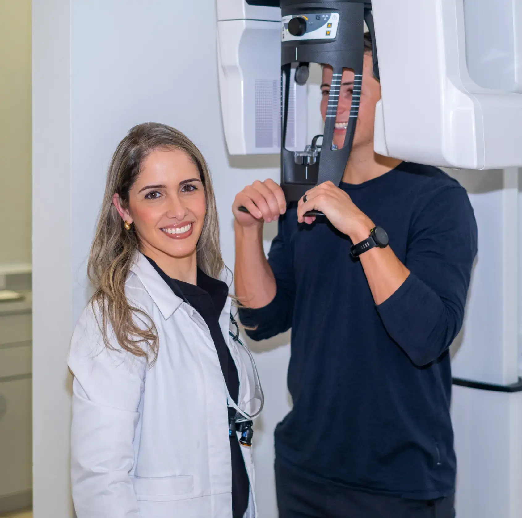 A dentist smiles while a patient gets a dental X-ray.