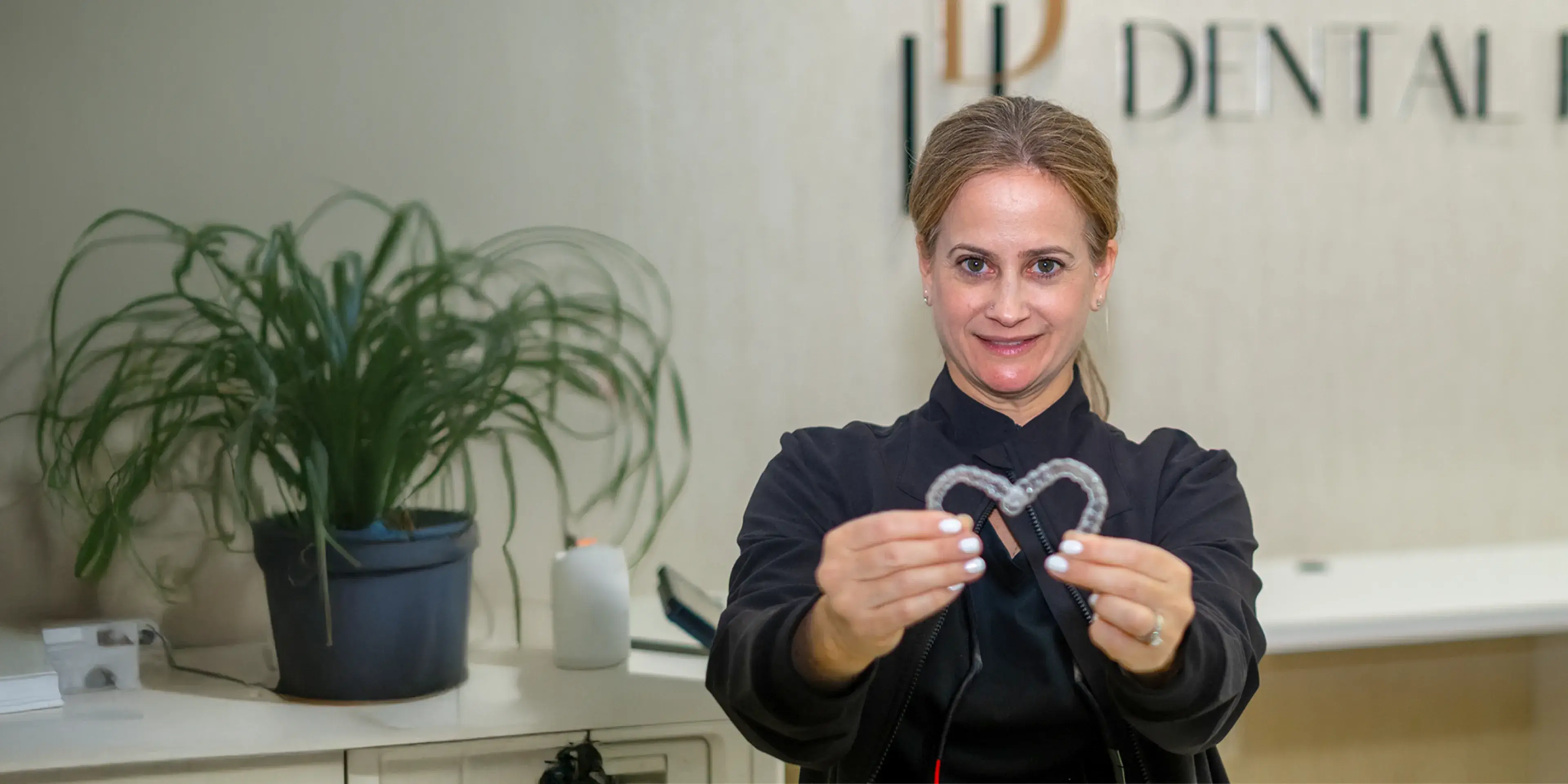 A person holds up a heart-shaped dental aligner in a dental office.