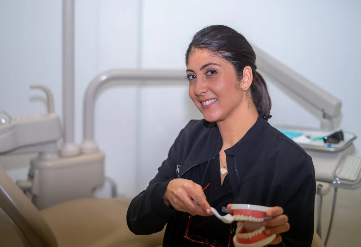 A dental professional smiling and demonstrating tooth brushing on a dental model.
