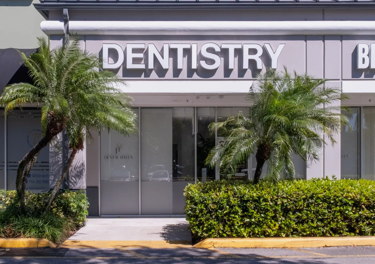 The image shows the front of a dentistry office with two palm trees outside.