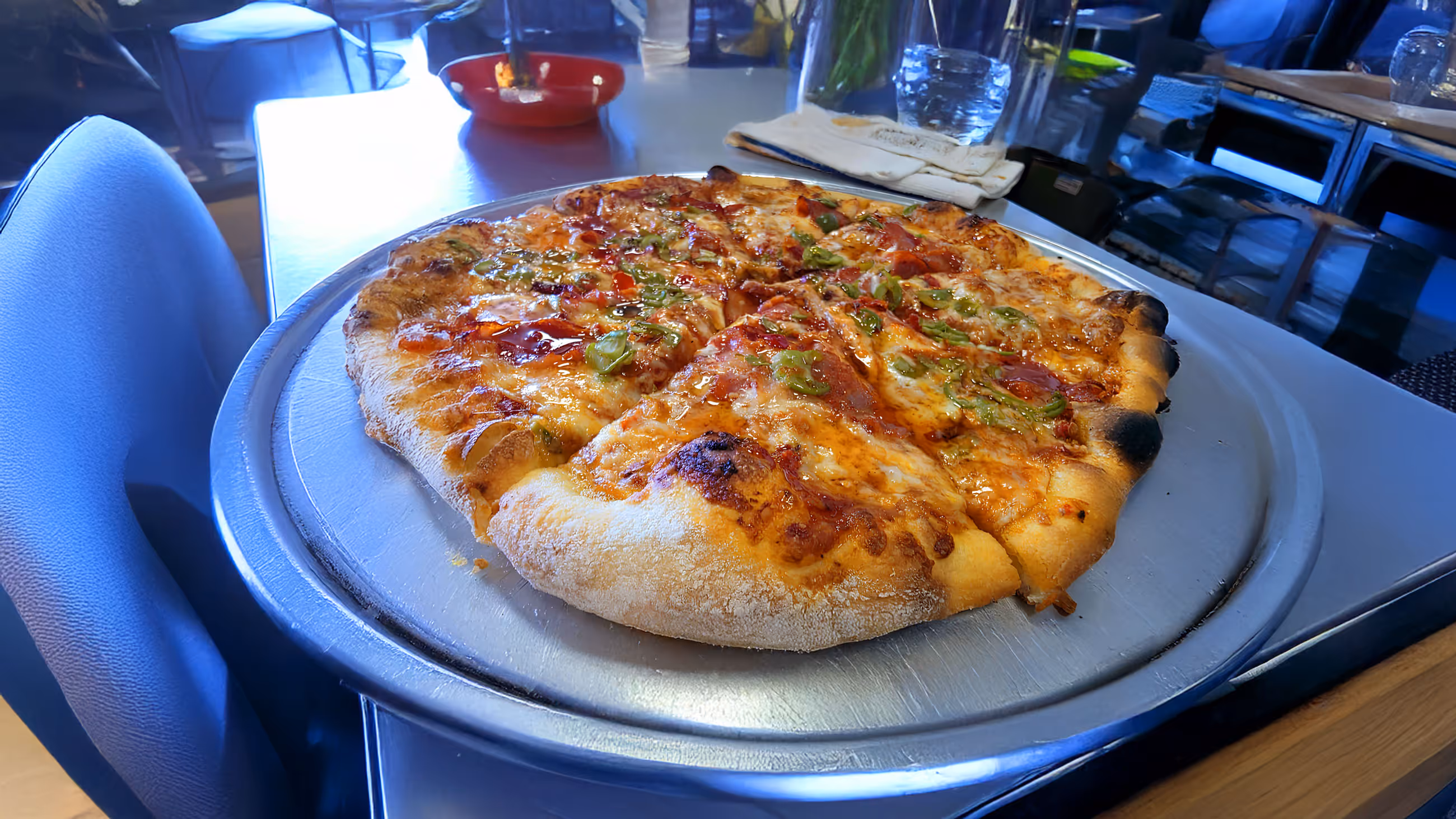 Pepperoni pizza with green peppers on a round metal tray on a table in a restaurant.