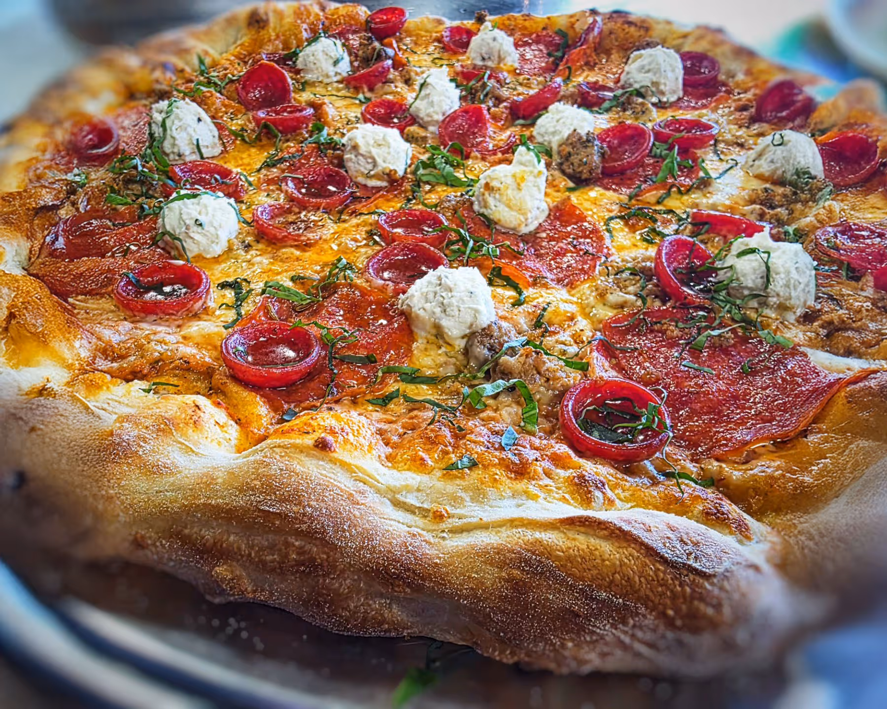 Close-up of a pepperoni pizza topped with dollops of ricotta cheese and fresh basil on a golden crust.