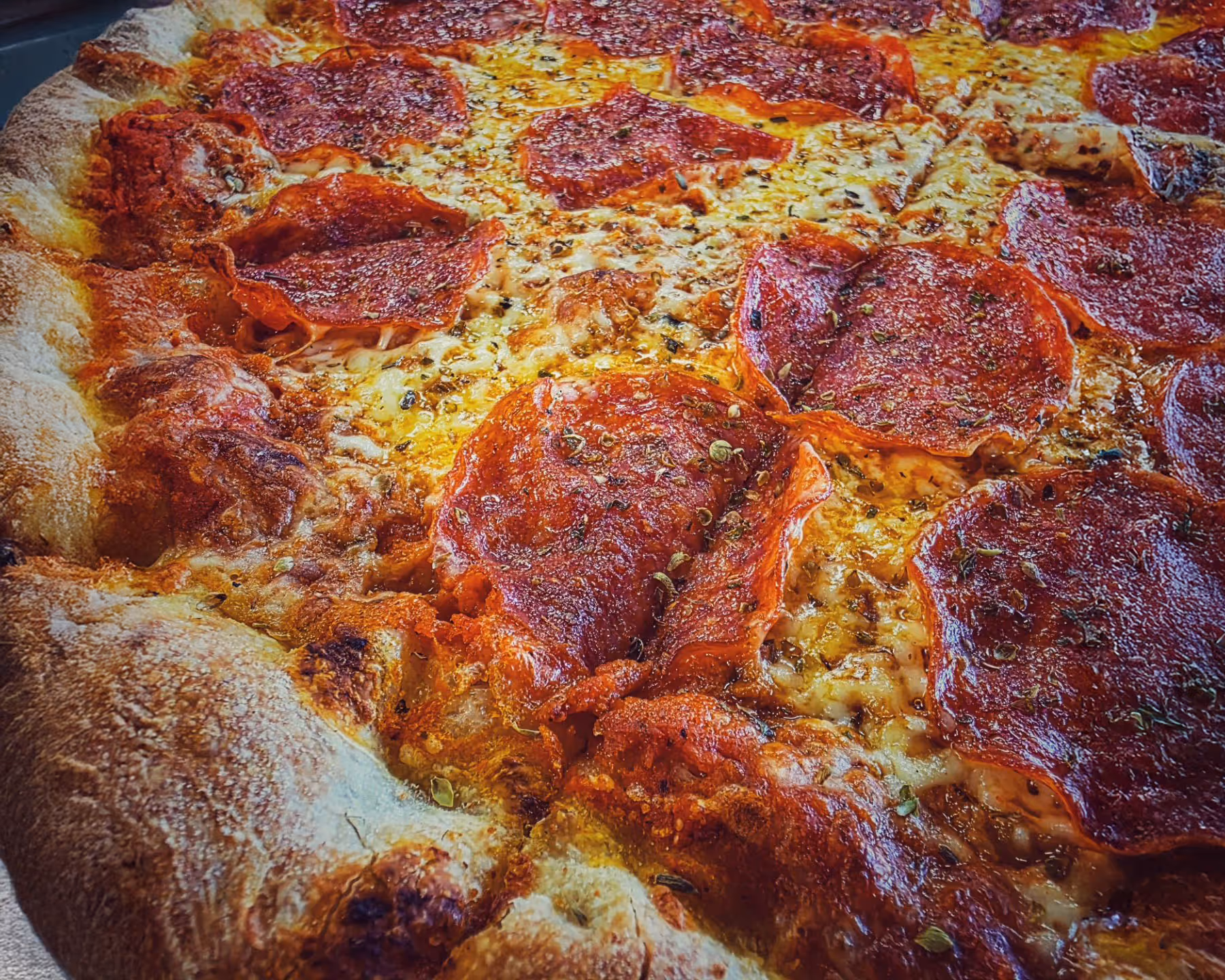 Person spreading red tomato sauce on pizza dough on a floured countertop in a kitchen.