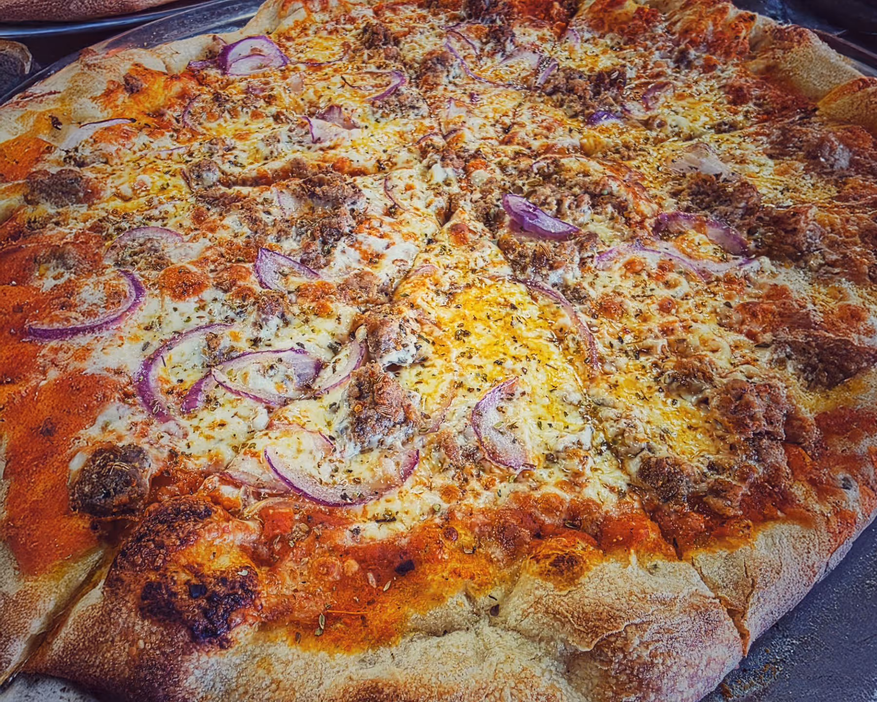 Large pizza with tomato sauce, melted cheese, ground meat, and sliced red onions on a crispy crust.