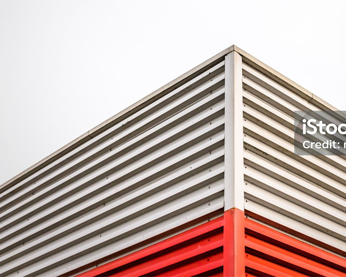 Corner of a building with horizontal white and red metal siding against a clear sky.