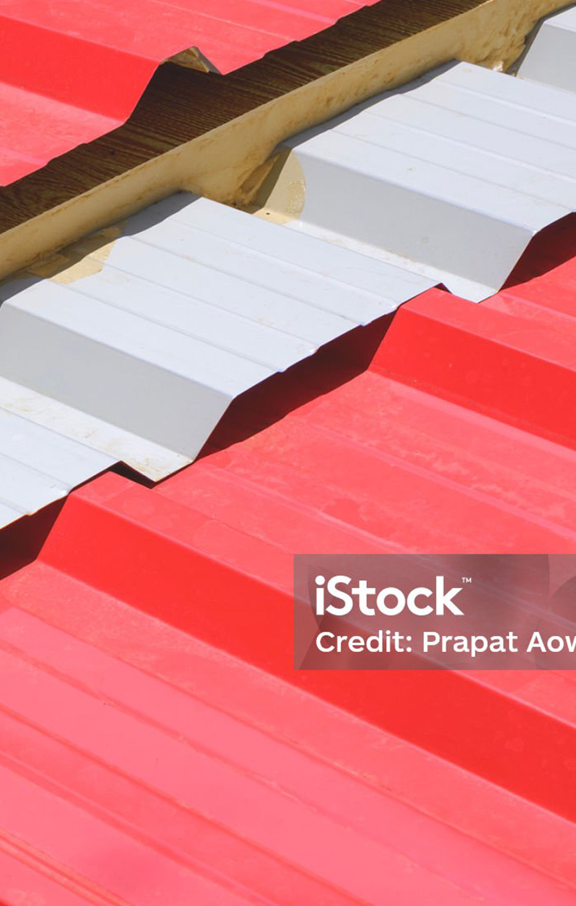 Close-up of red and white corrugated metal roofing panels with foam insulation between them.