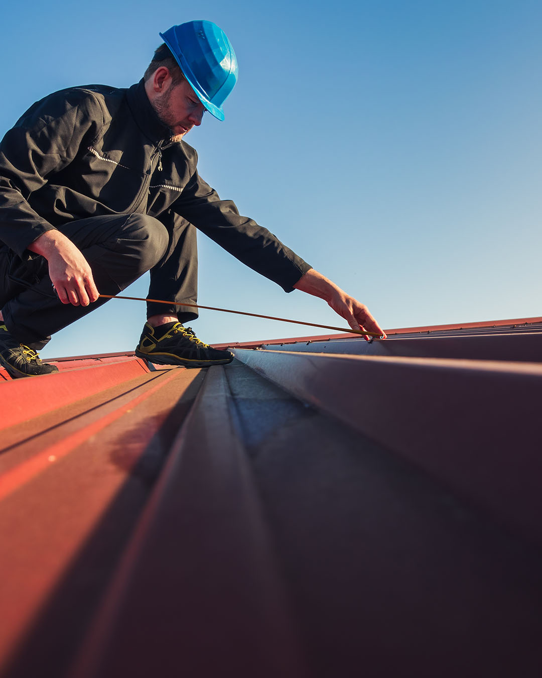 A photo of a roofing professional using a measuring tape to measure the metal cladding on a roof.